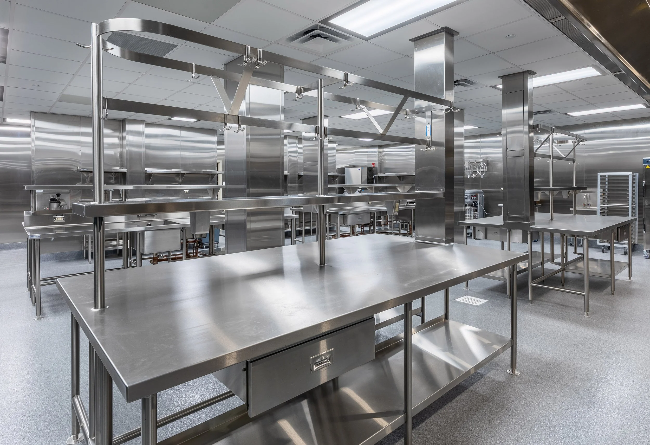 A spacious, modern commercial kitchen with stainless steel counters, shelving, and appliances. The clean, brightly lit interiors feature multiple workstations and industrial fixtures—ideal for dietary needs in healthcare settings.
