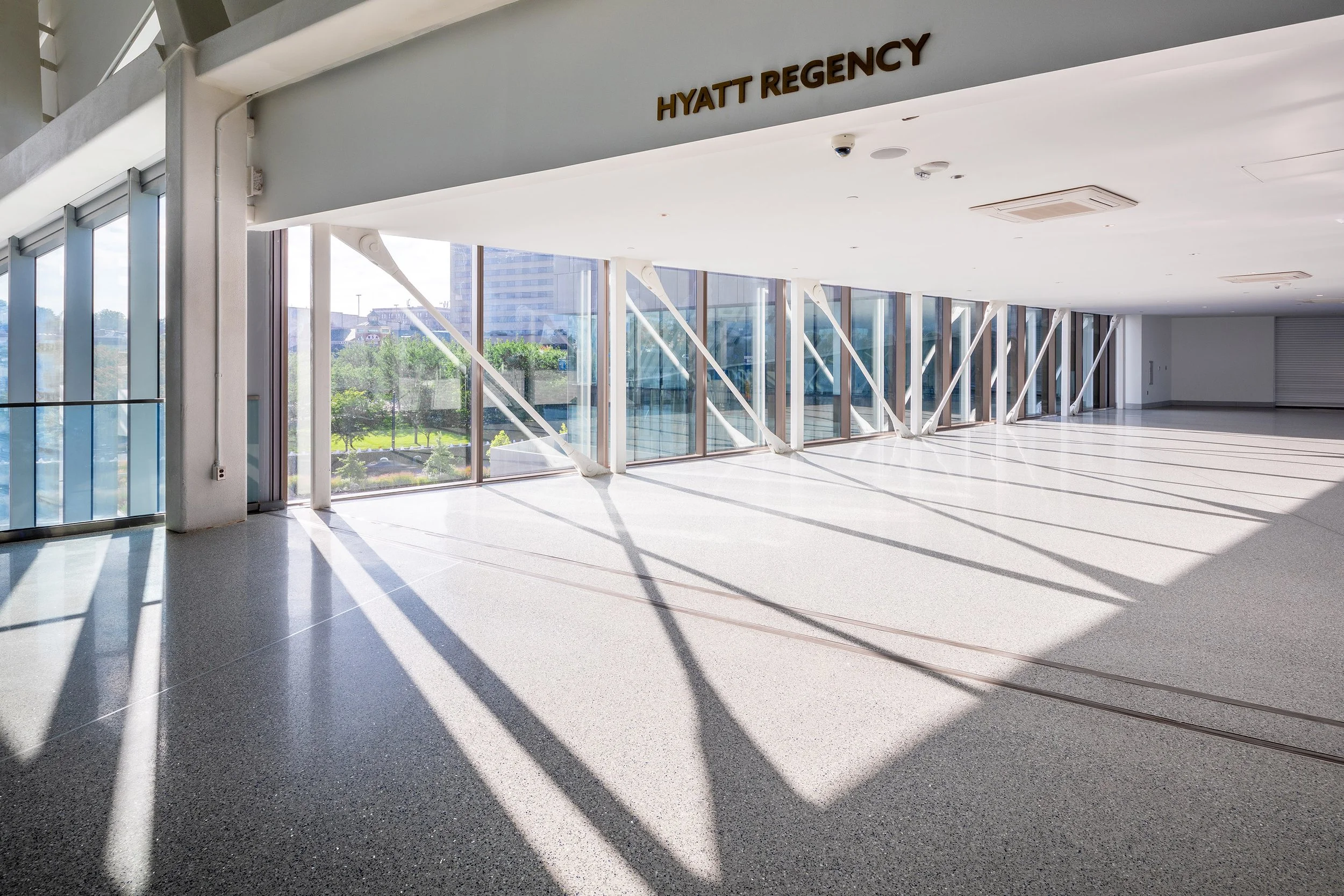 Spacious, sunlit hallway with terrazzo floors and Hyatt Regency sign above the entrance. Shadows stretch across this elegant installation.
