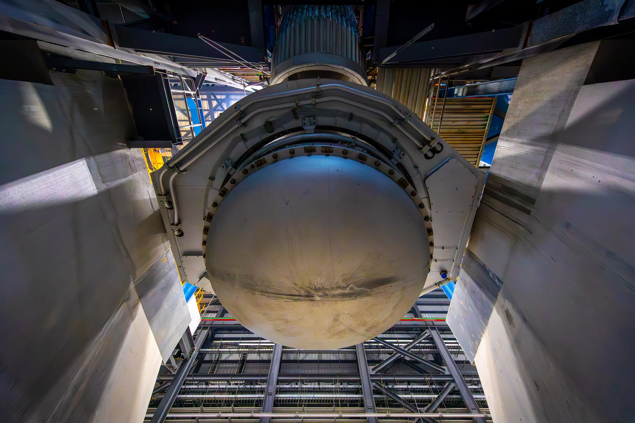 Close-up view from below of a large melter, surrounded by industrial metal framework and structural supports inside an industrial facility. The photography highlights the size and complexity of the engineering.