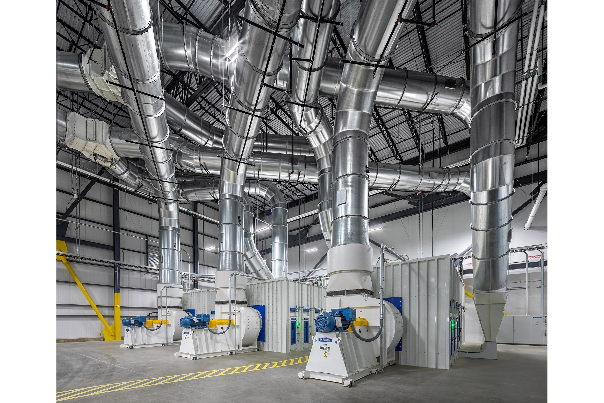 Large industrial facility interior with massive polished metal ductwork and several large ventilation machines on the floor.