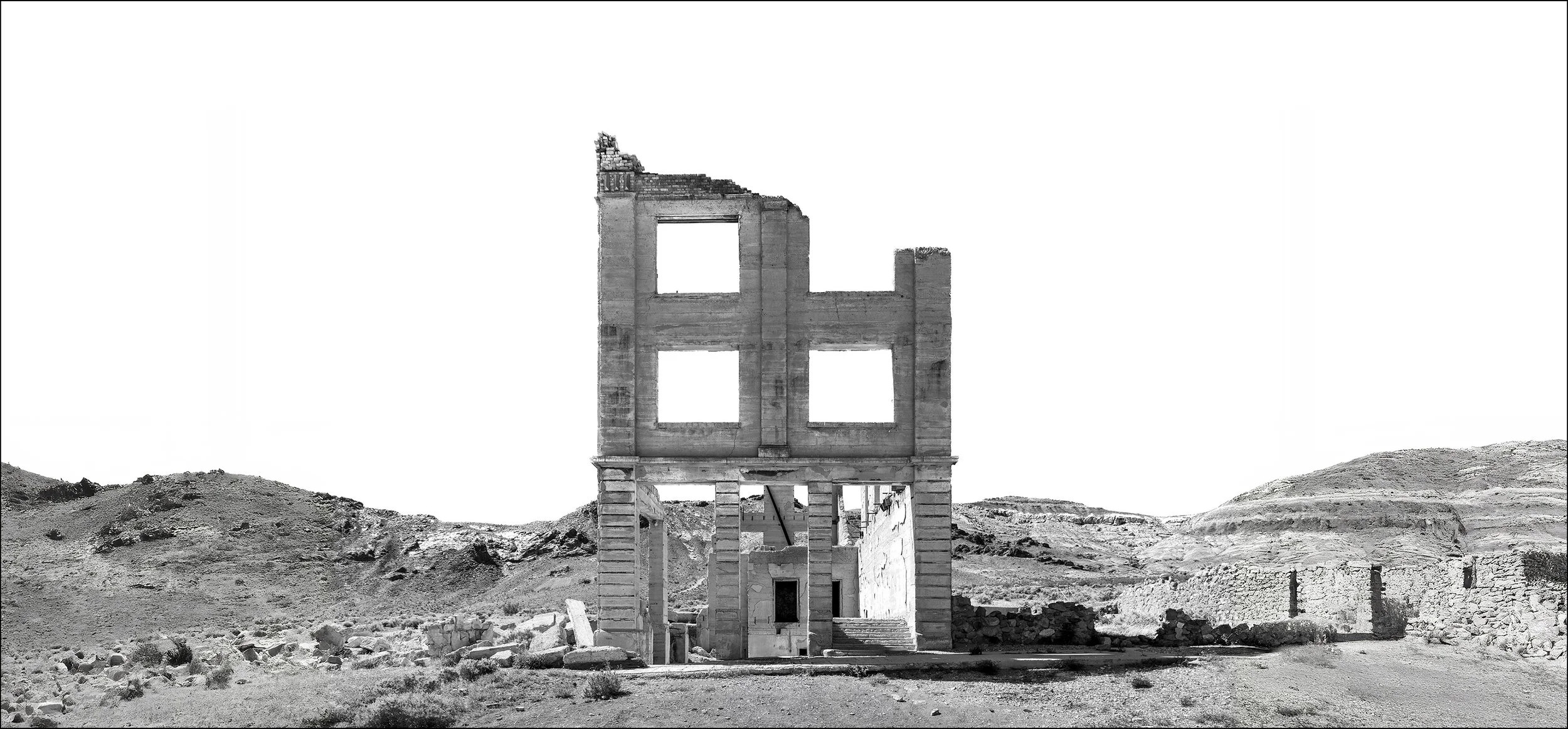 Ruins of stone building in Rhyolite near death valley with desert and clear white sky.