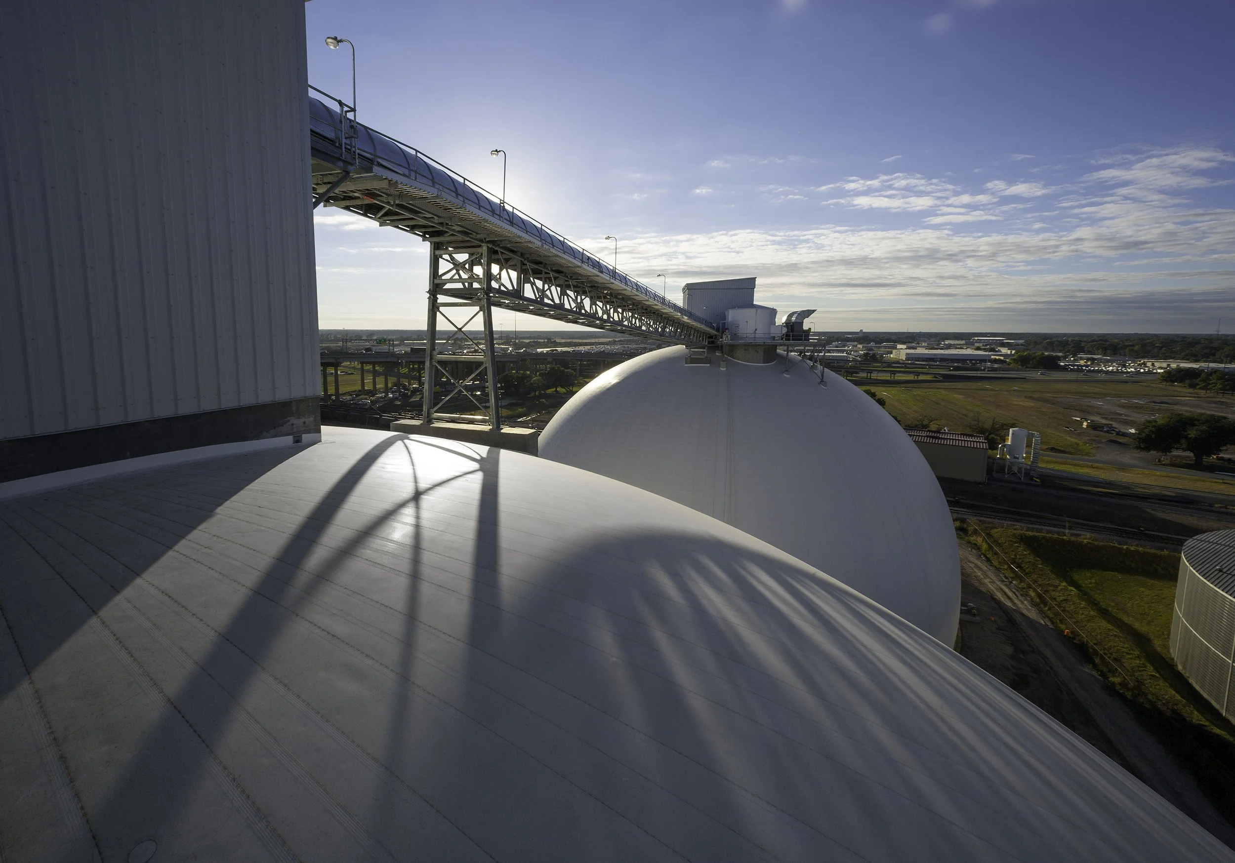 Large white industrial domes and elevated conveyor belts under a blue sky at an industrial facility.