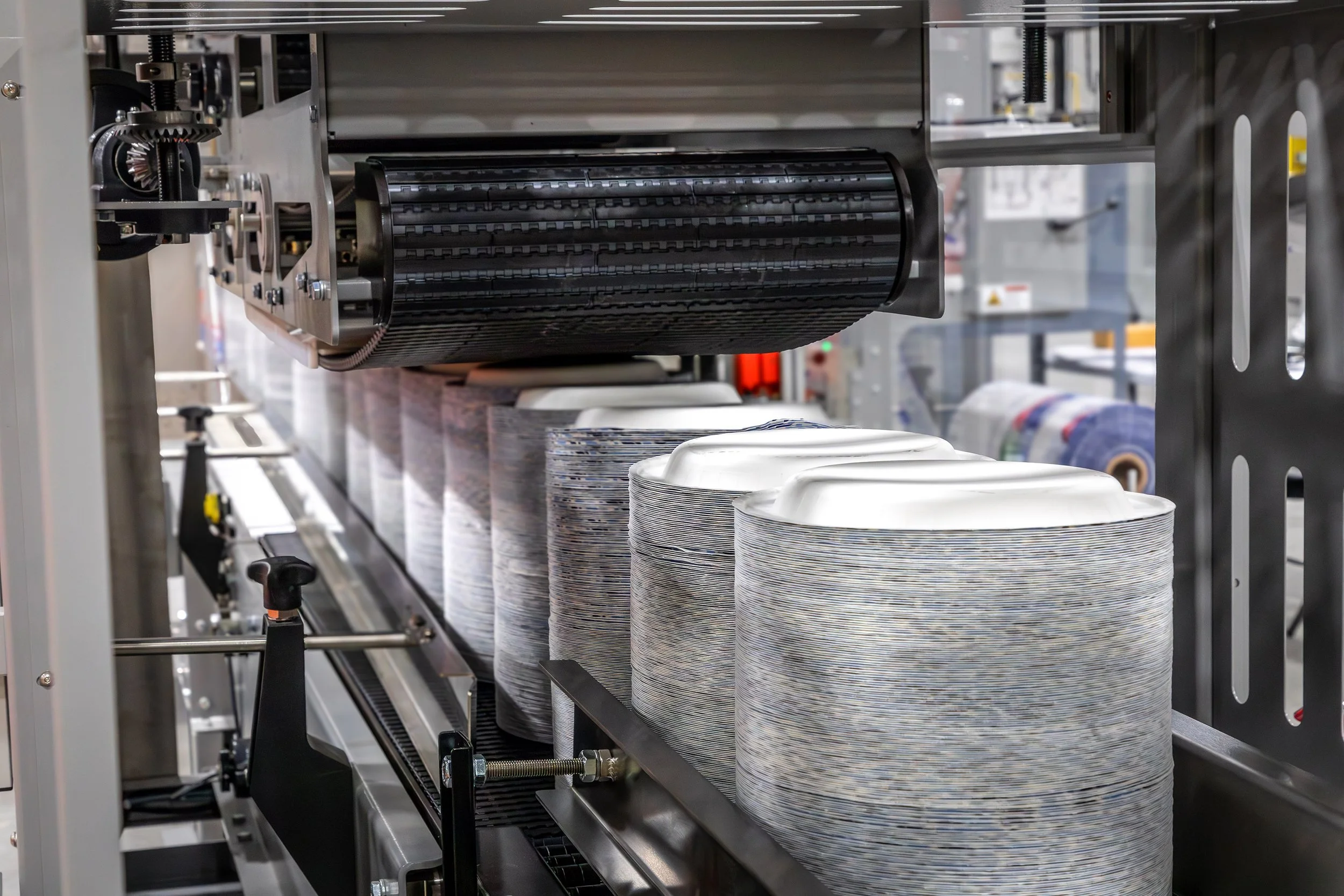 Close-up of an industrial machine stacking multiple rows of paper plates in a manufacturing facility.