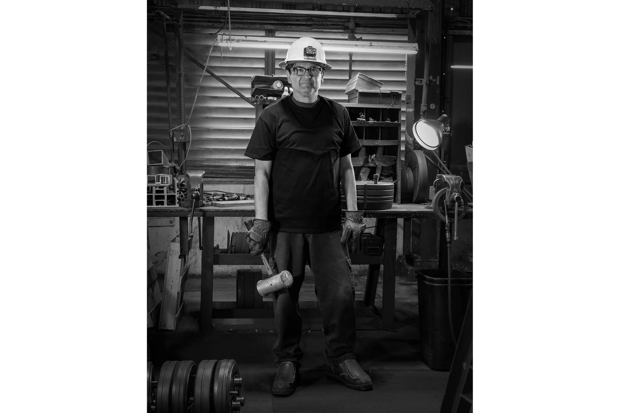 A workforce member in a hard hat holds a mallet, standing amidst aluminum structures in an industrial machine shop.