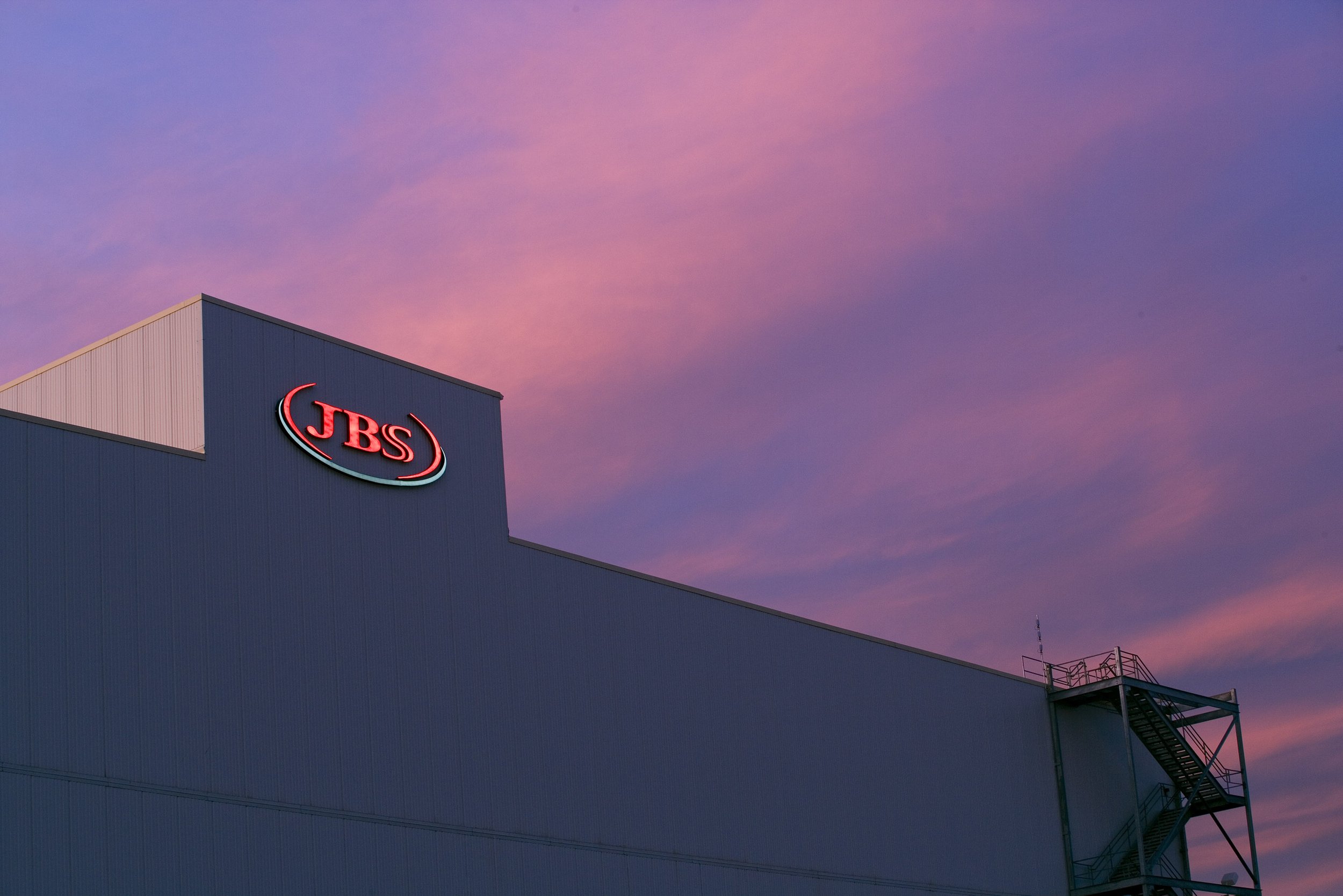 A JBS building in Texas with an exterior staircase glows beneath a pink and purple sunset sky.