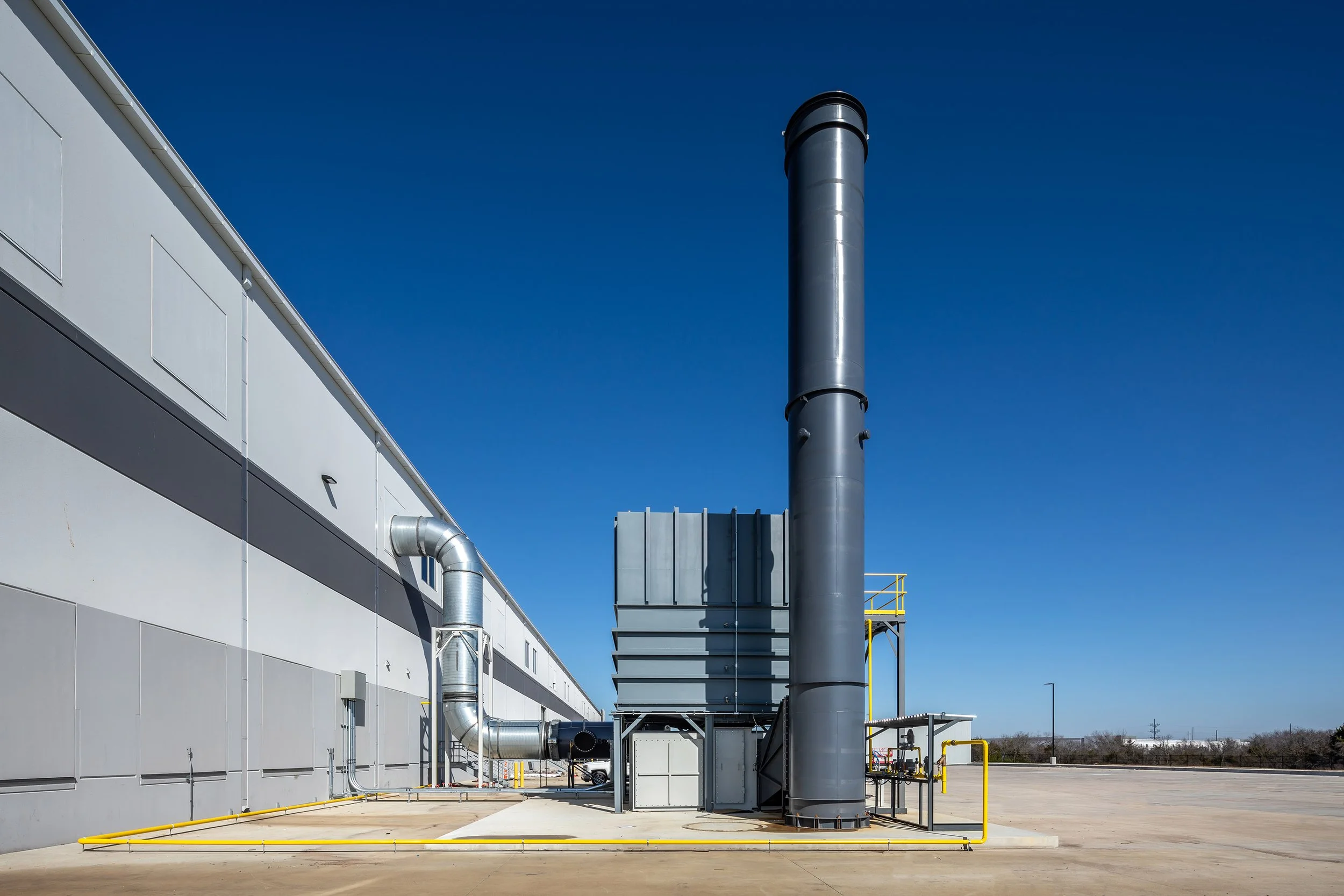 A large grey smokestack stands outside of an industrial building in Dallas, Texas.
