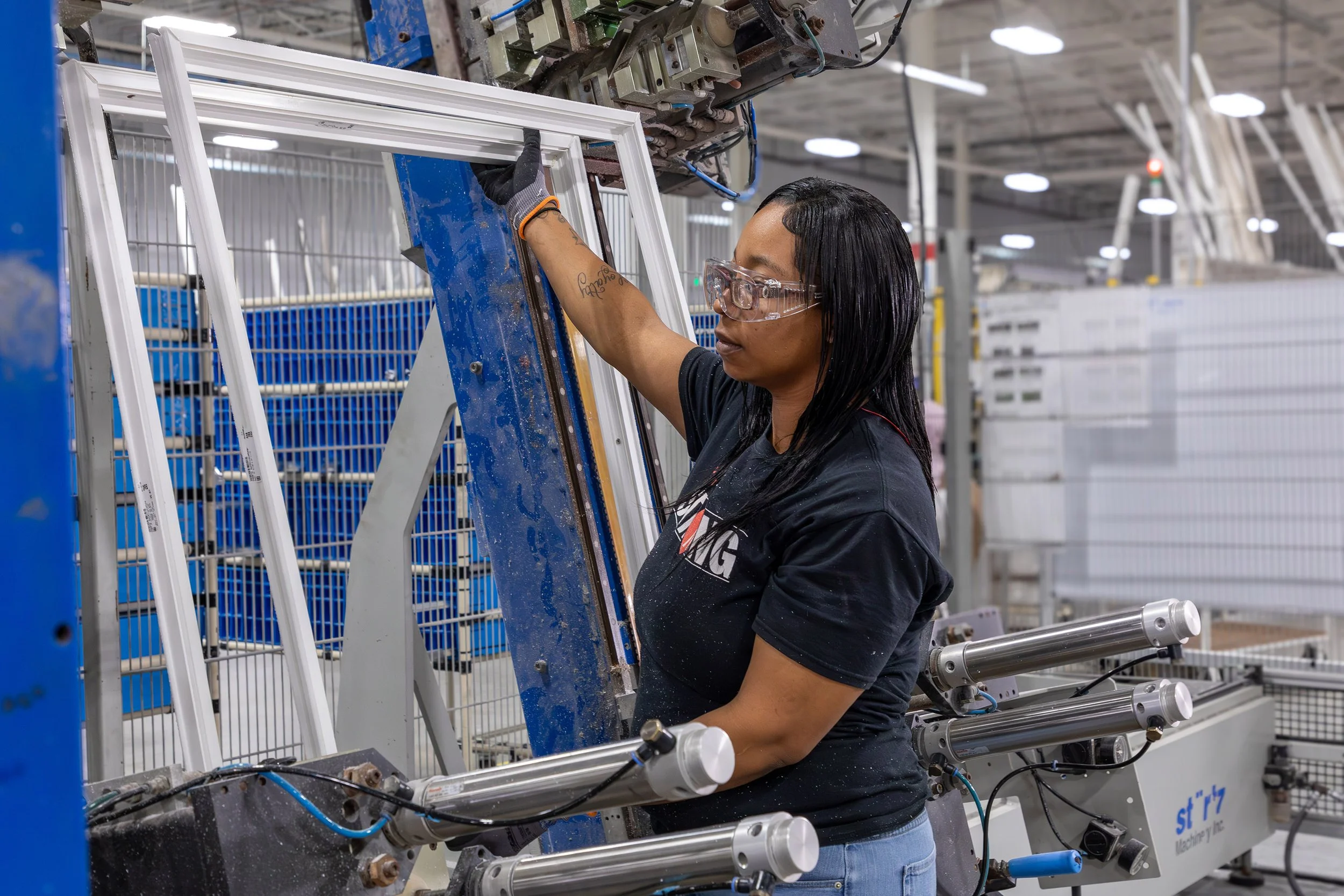 A woman wearing safety glasses operates machinery to assemble a window frame at an industrial manufacturer in Macon.