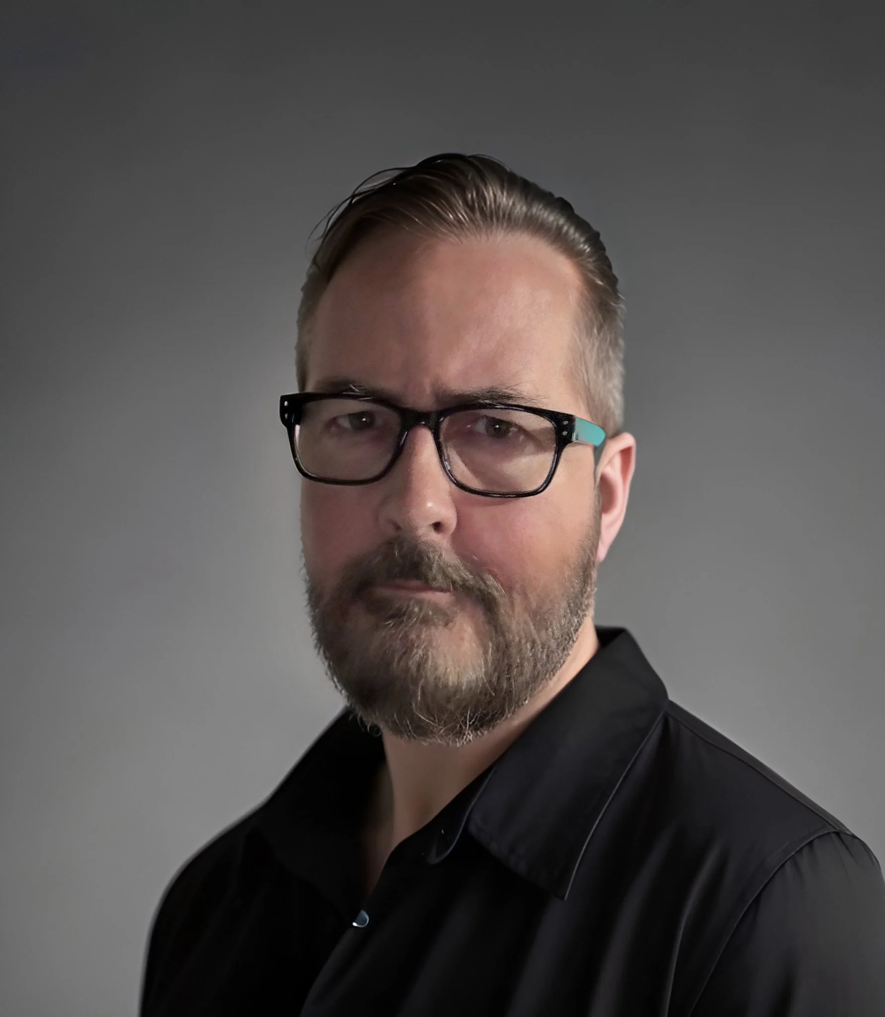 Tim Arvin, a man with glasses and a beard wearing a black shirt against a gray background.