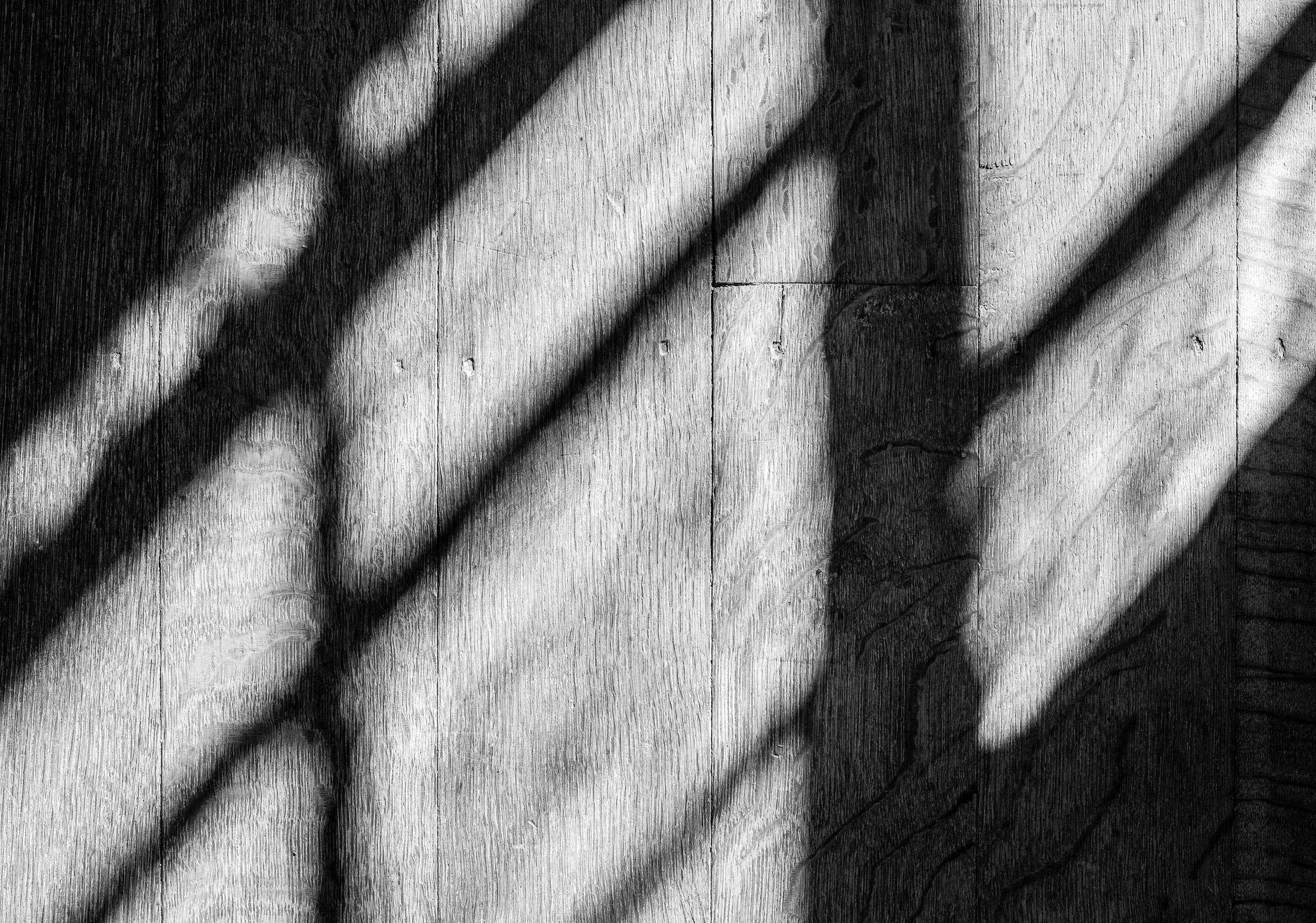 Sunlight casting diagonal shadows across a Shaker wood floor, creating a high-contrast winter pattern.