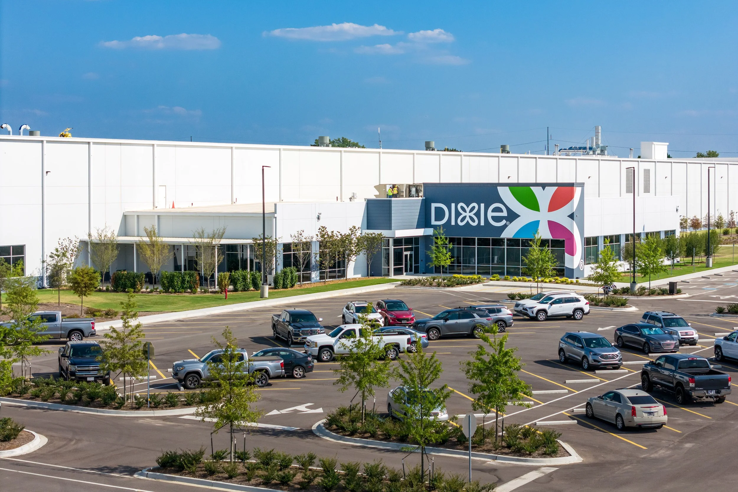 A large white industrial building with a Dixie mural sign and colorful logo, surrounded by a parking lot with several cars.