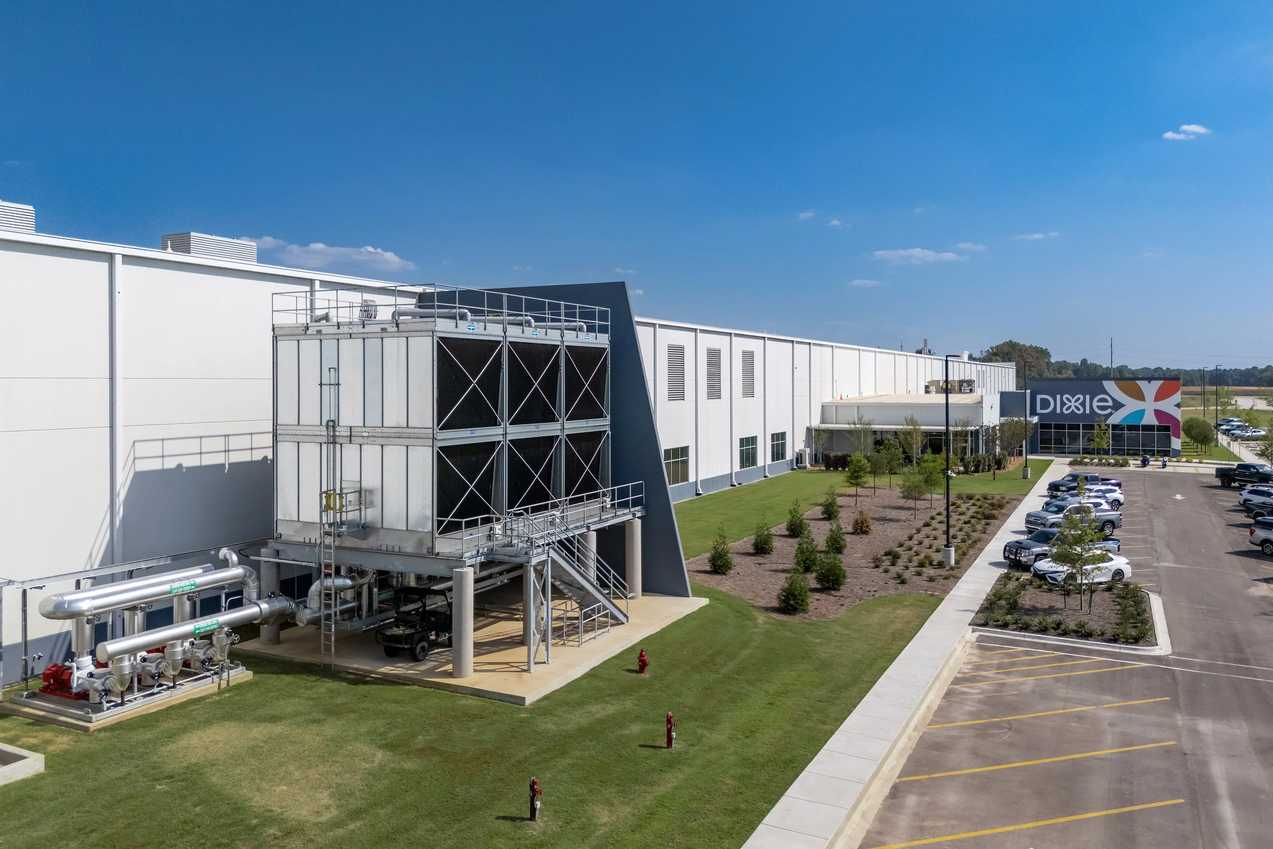 A modern architectural facility with a cooling system, landscaped lawn, and Dixie sign manufactures paper products under a clear sky.