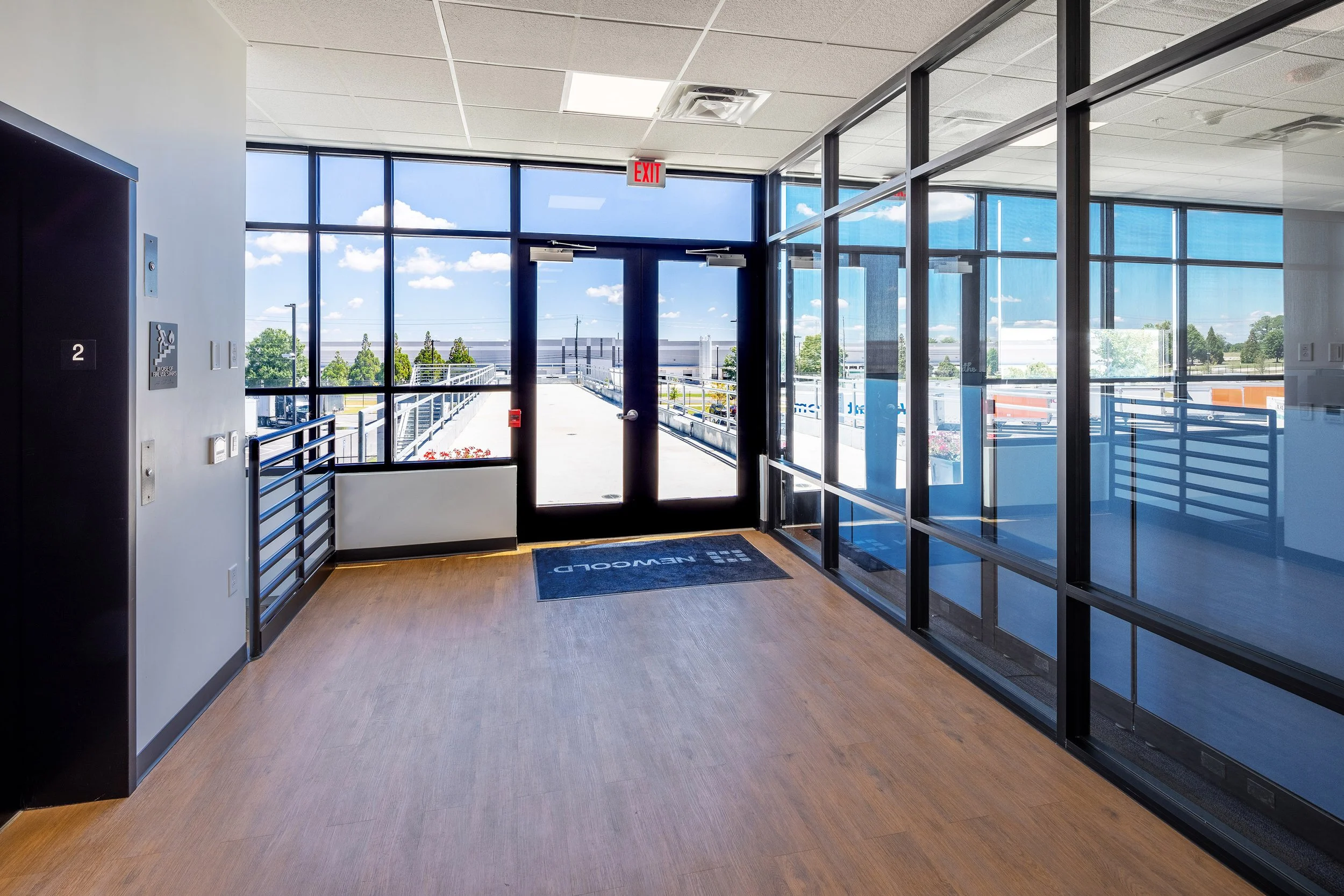 Modern second-floor hallway with wood flooring and glass walls; daylight streams in through large Georgia windows.