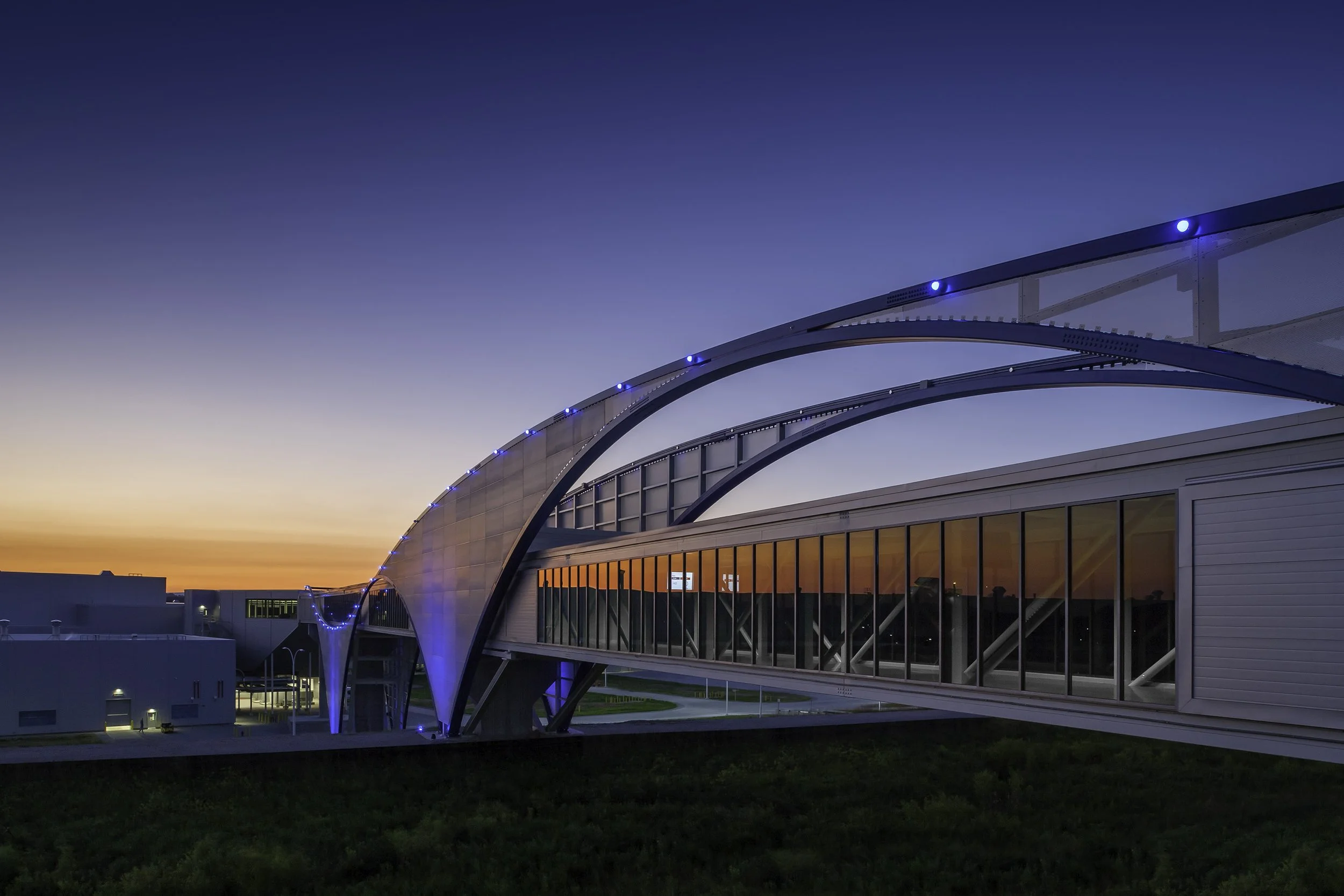 Modern skybridge at Volkswagen Plant with glass walls and blue lights at sunset.