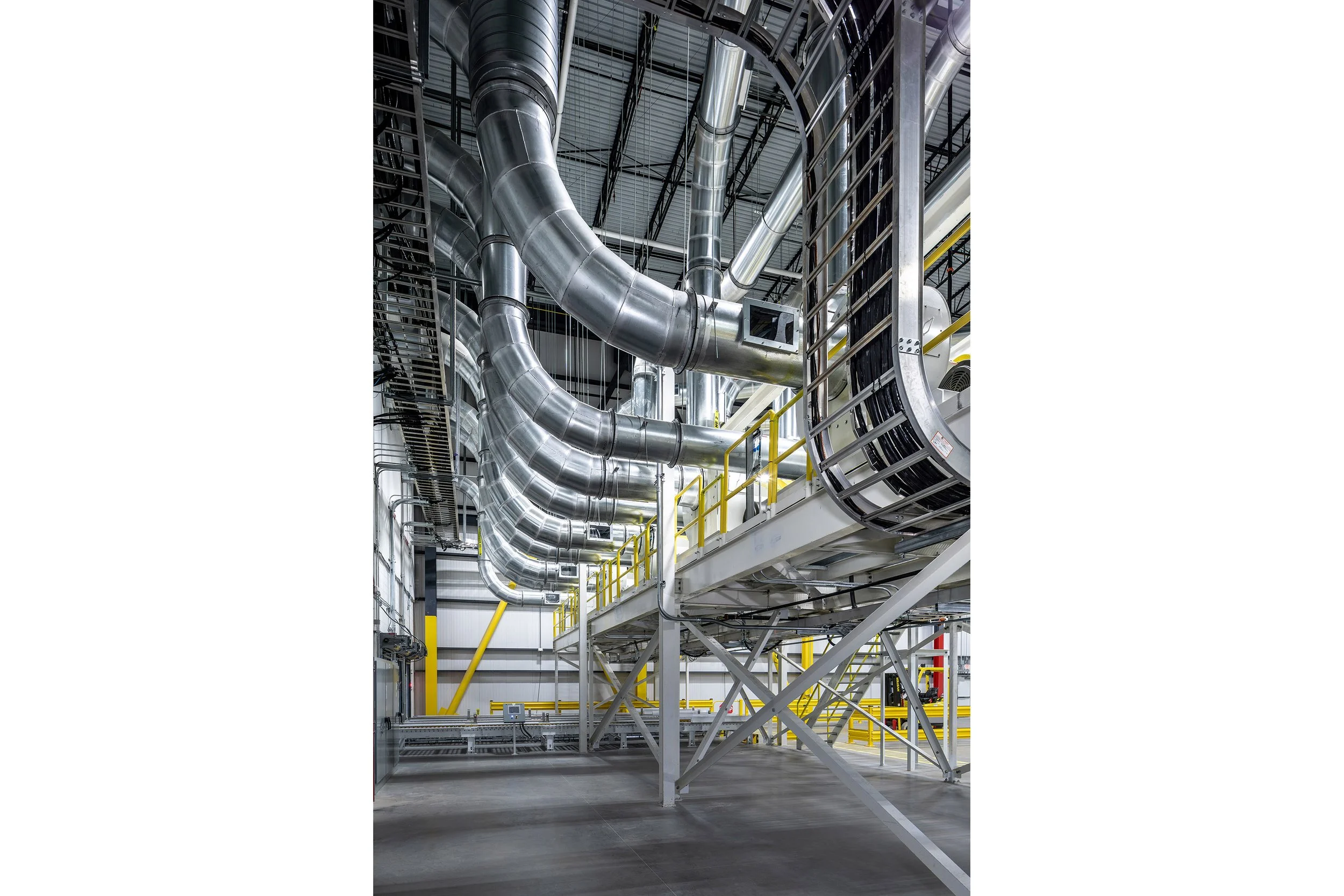 Large industrial interior with metal ducts, pipes, and platforms, featuring yellow railings and structural beams.