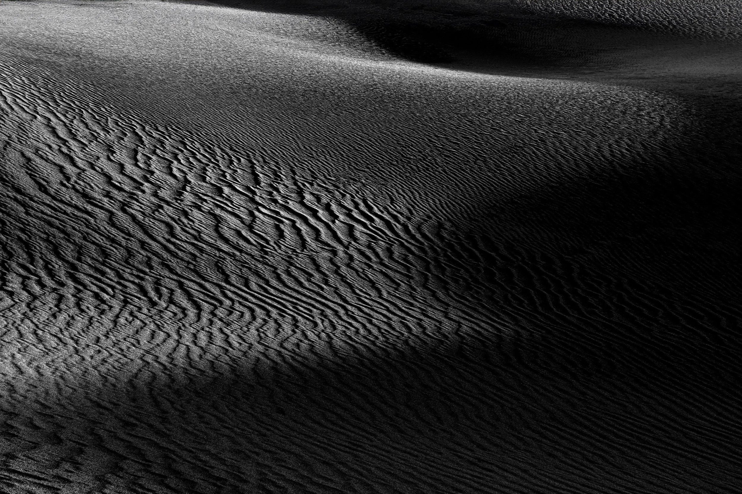 Black and white photo of Death Valley sand dunes with textured ripples and smooth, shadowed curves.
