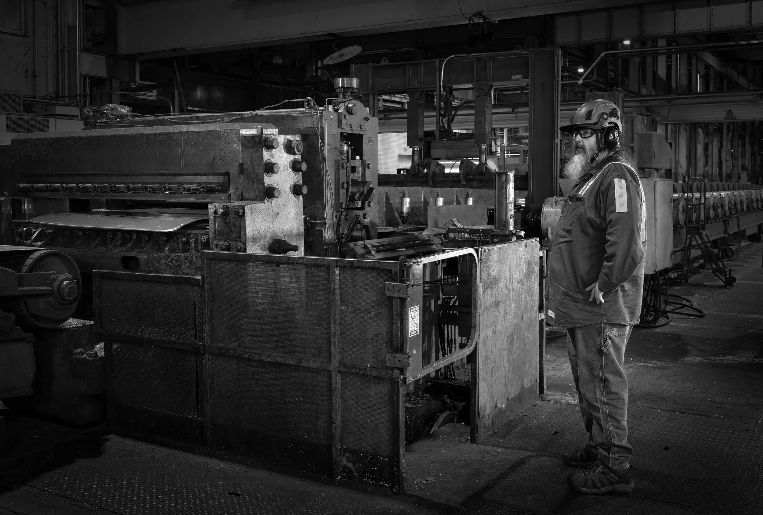 A worker in safety gear operates industrial machinery, showcasing the art of a skilled workforce inside a large manufacturing plant.