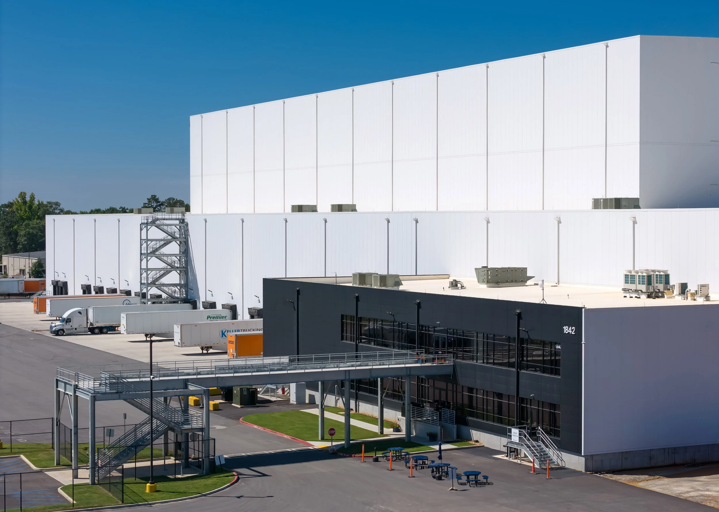 Large white industrial warehouse with refrigeration, loading docks, and trucks in Georgia under a clear blue sky.