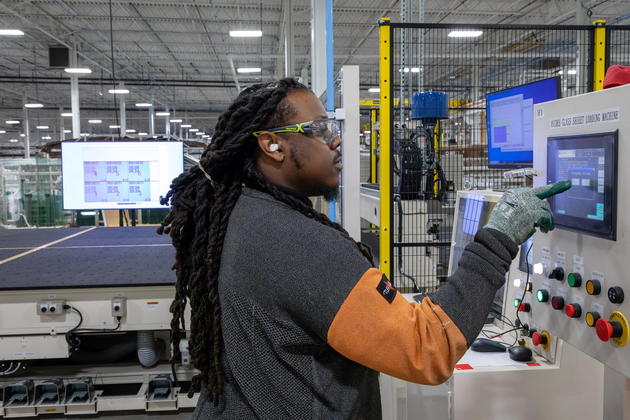 A worker operates a touchscreen control panel in an industrial manufacturing facility.
