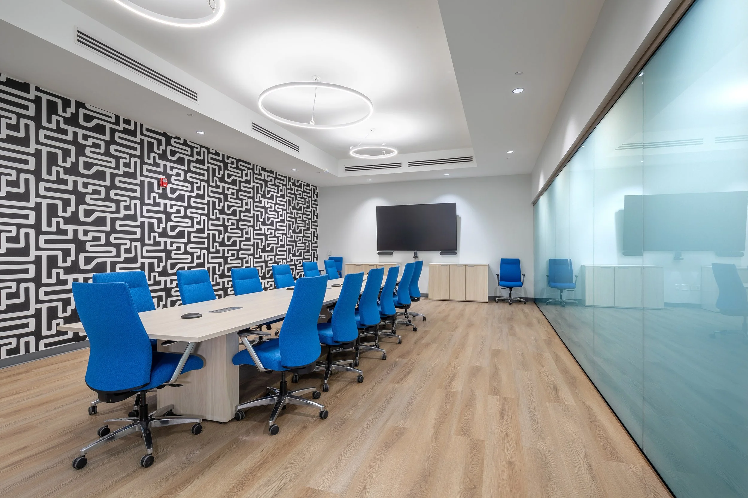 Modern luxurious conference room with a long table, blue chairs, wall-mounted screen, and wood flooring.