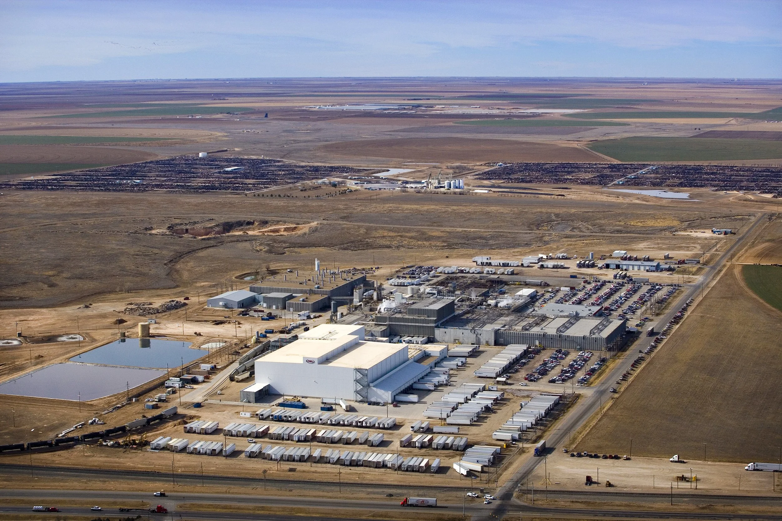 A large Texas industrial complex surrounded by dry fields and parking lots, hinting at a massive food process facility in the distance.