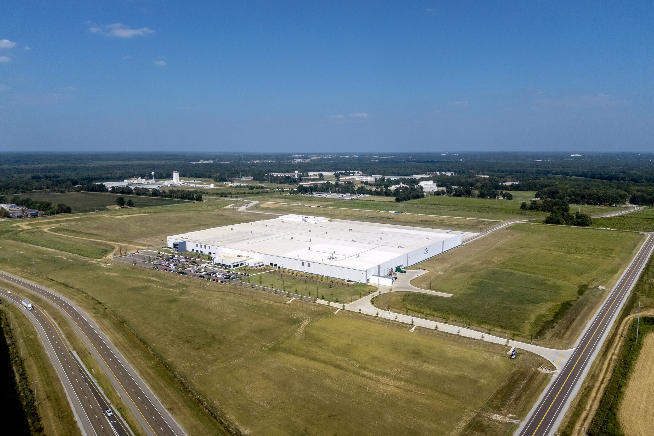 A large white Georgia Pacific industrial building surrounded by grassy fields, roads, and parking lots under a clear blue sky.