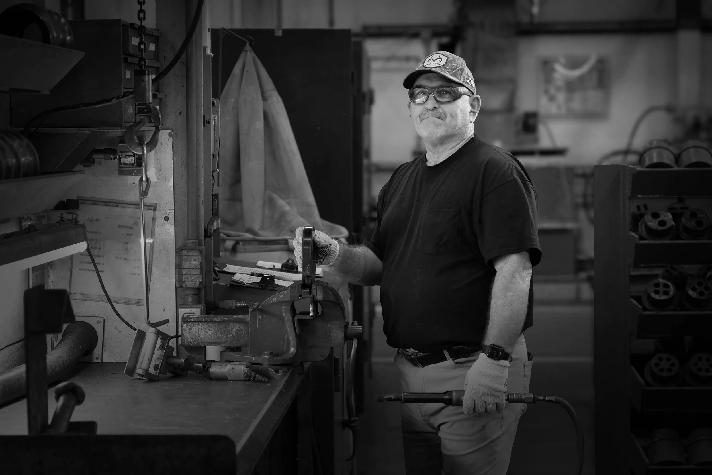 A man in work clothes and gloves stands by industrial aluminum equipment in a factory, looking at the camera.