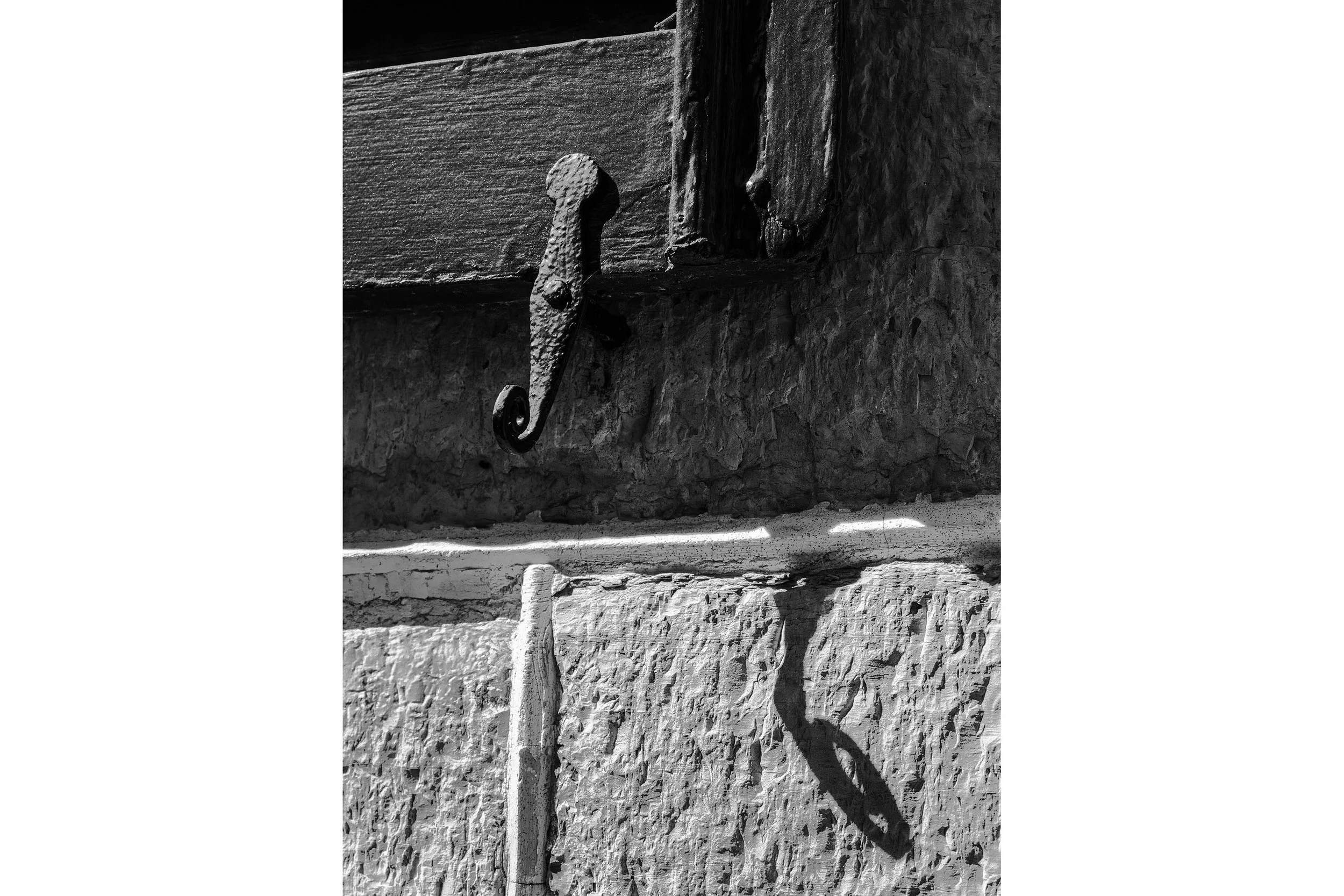 A metal latch casts a shadow on a textured stone wall of a historic building in black and white.