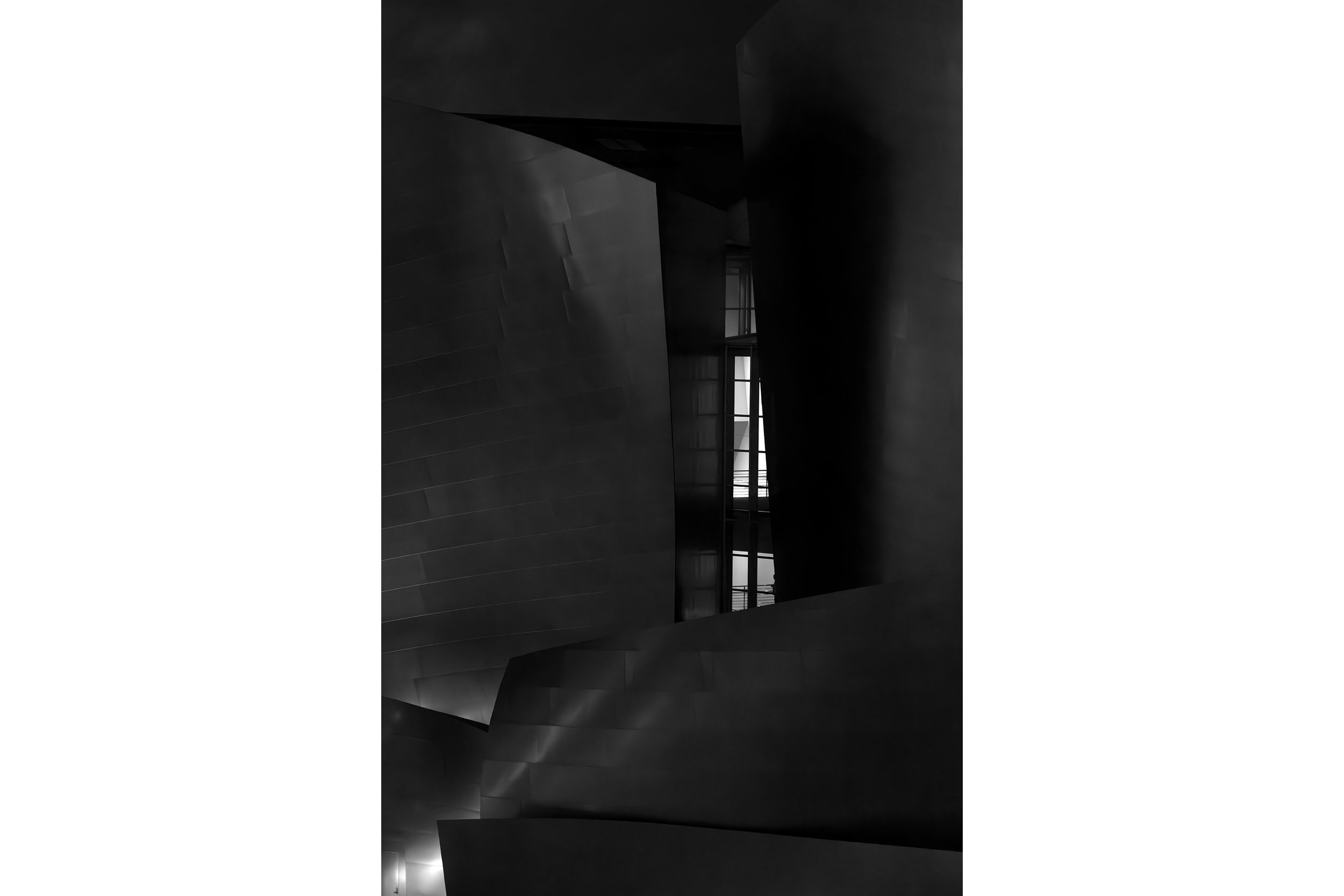 Abstract black and white photo of a modern building with geometric shapes and a vertical window at night.