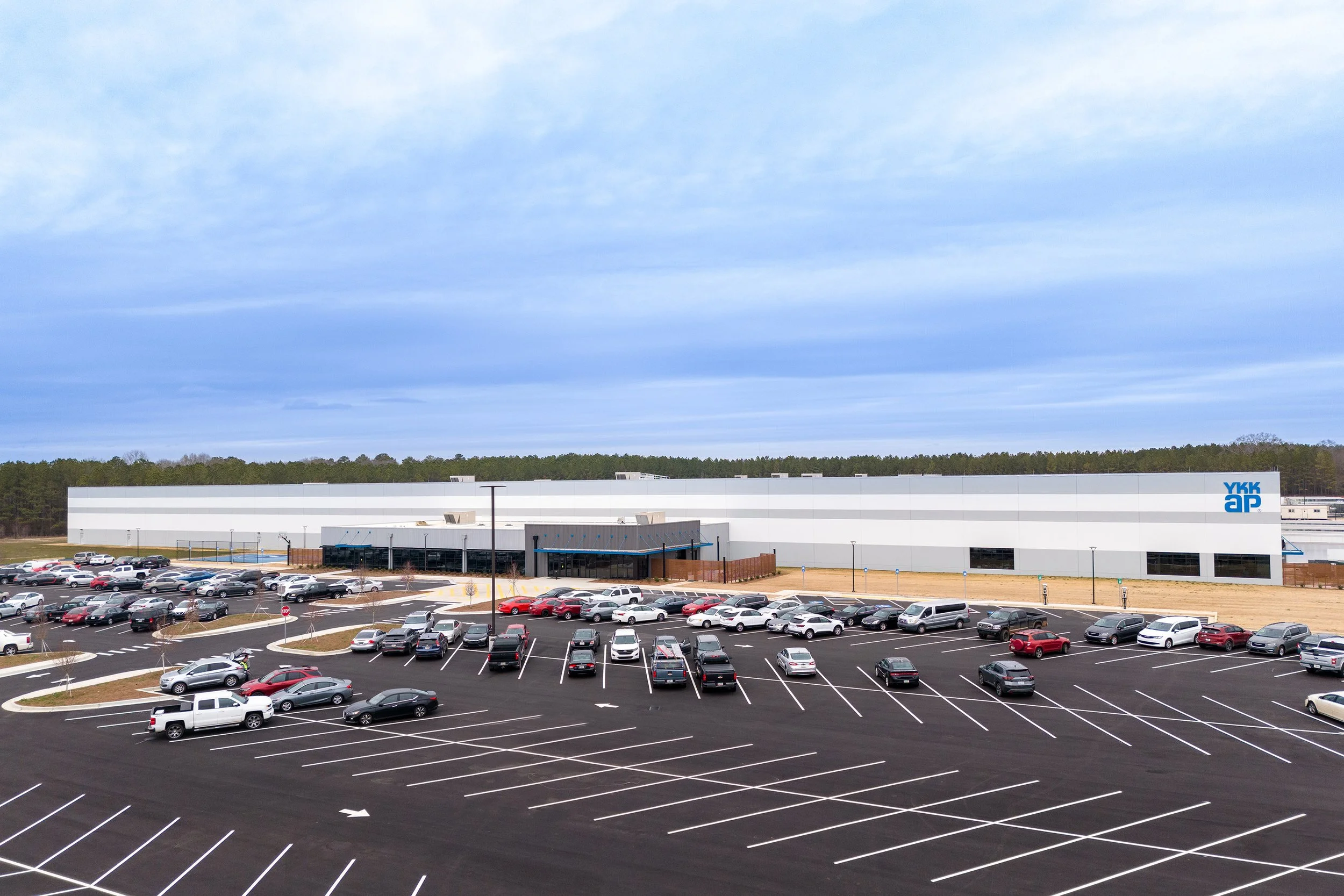 Large industrial building in Georgia with many parked cars in front, under a cloudy sky and surrounded by trees.
