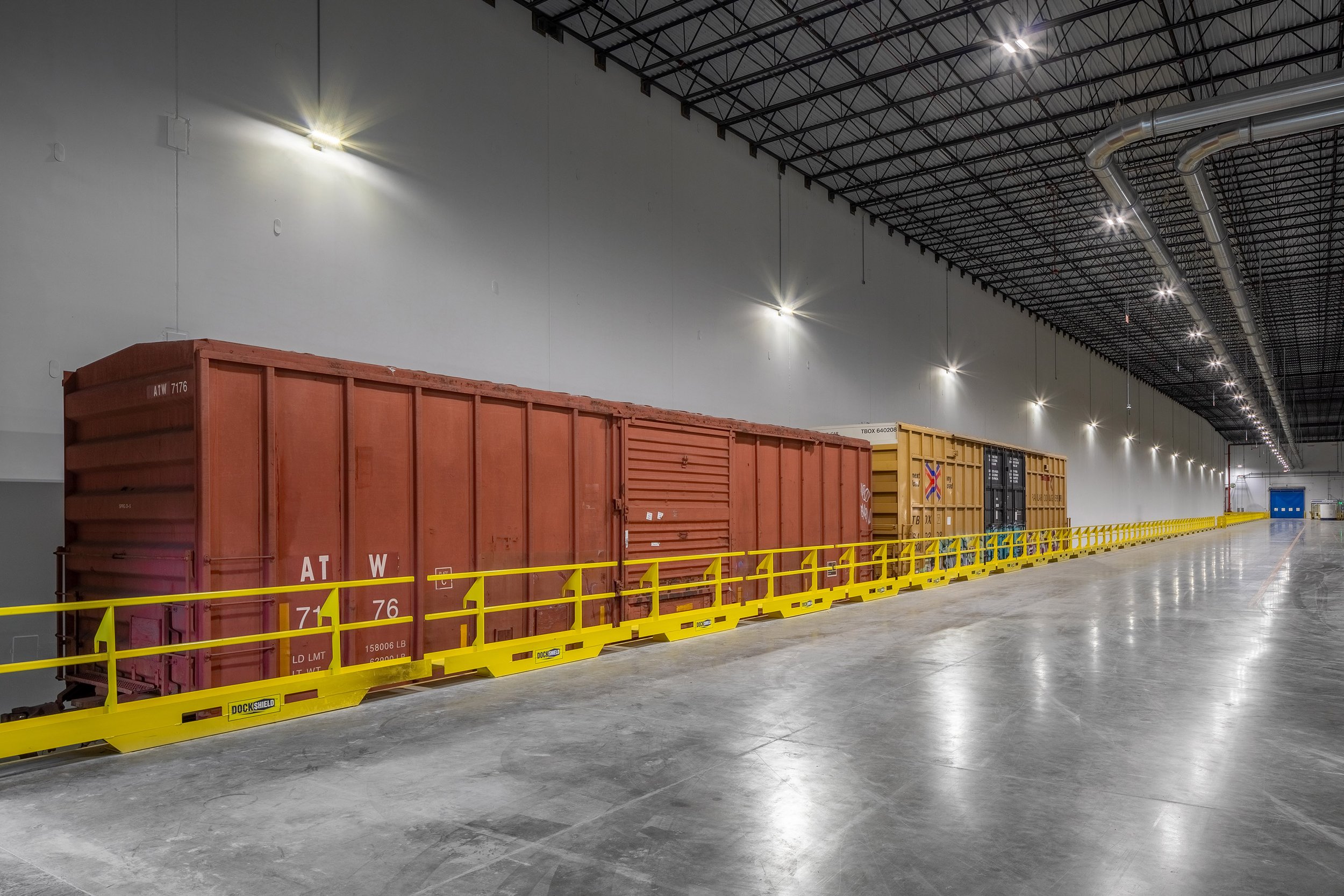 Freight train boxcars are parked inside a large, well-lit Georgia Pacific warehouse with yellow safety railings.