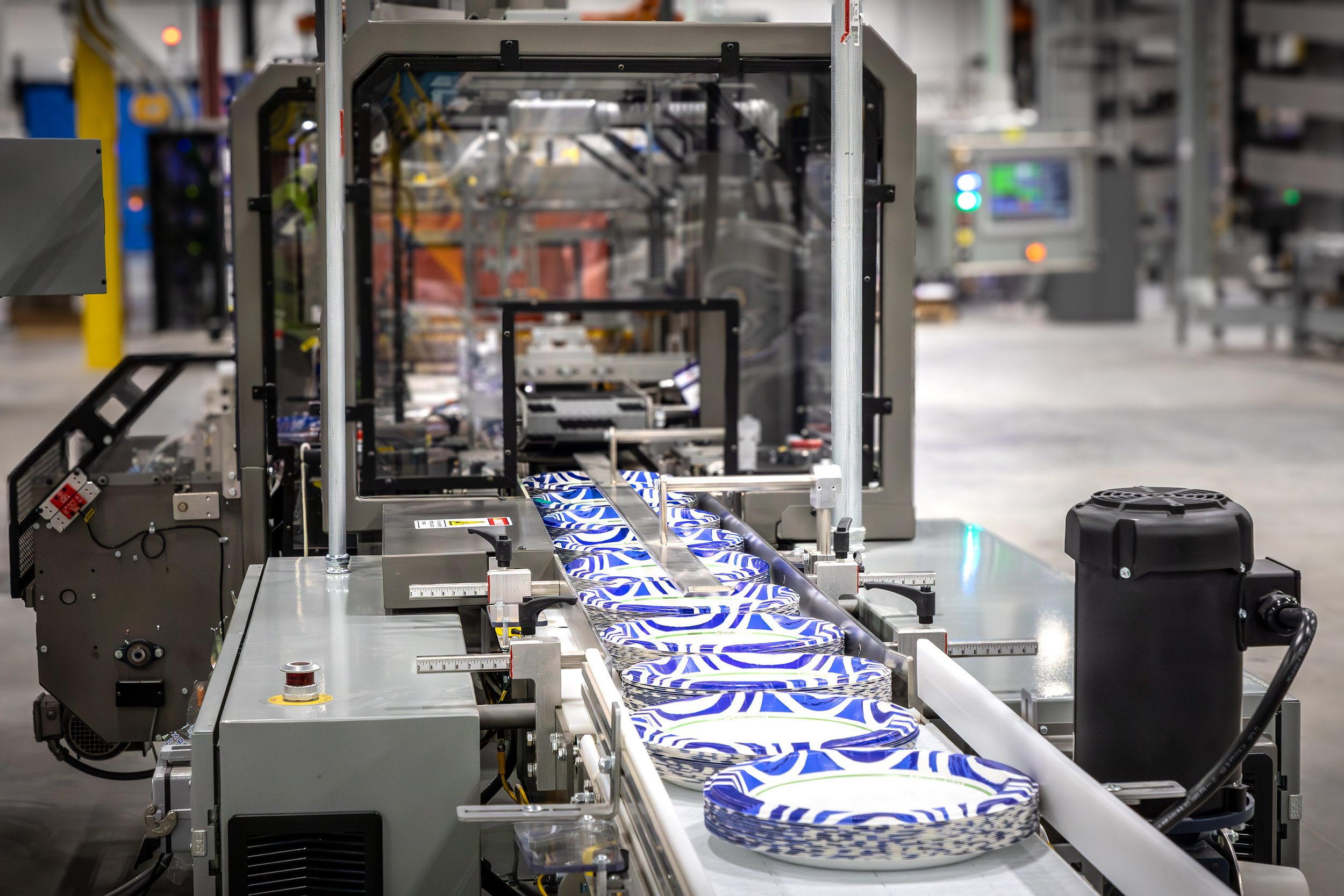 A conveyor belt moves stacks of Dixie paper plates through automated packaging process.