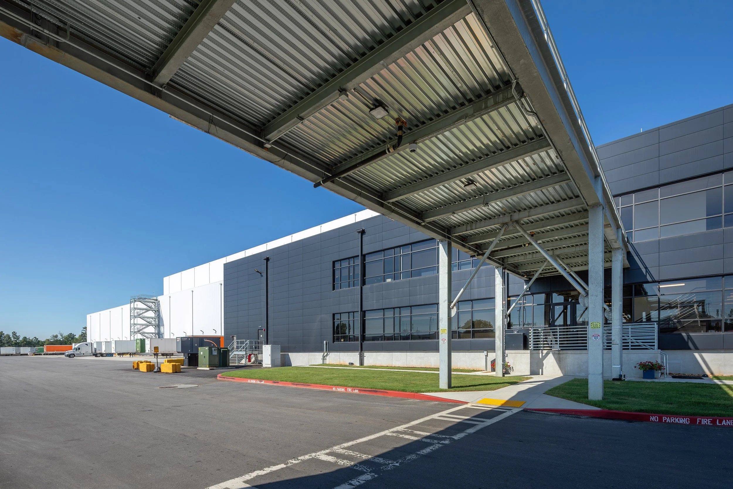 A modern industrial building with gray metal siding, a covered walkway, and a clear blue Georgia sky in the background.