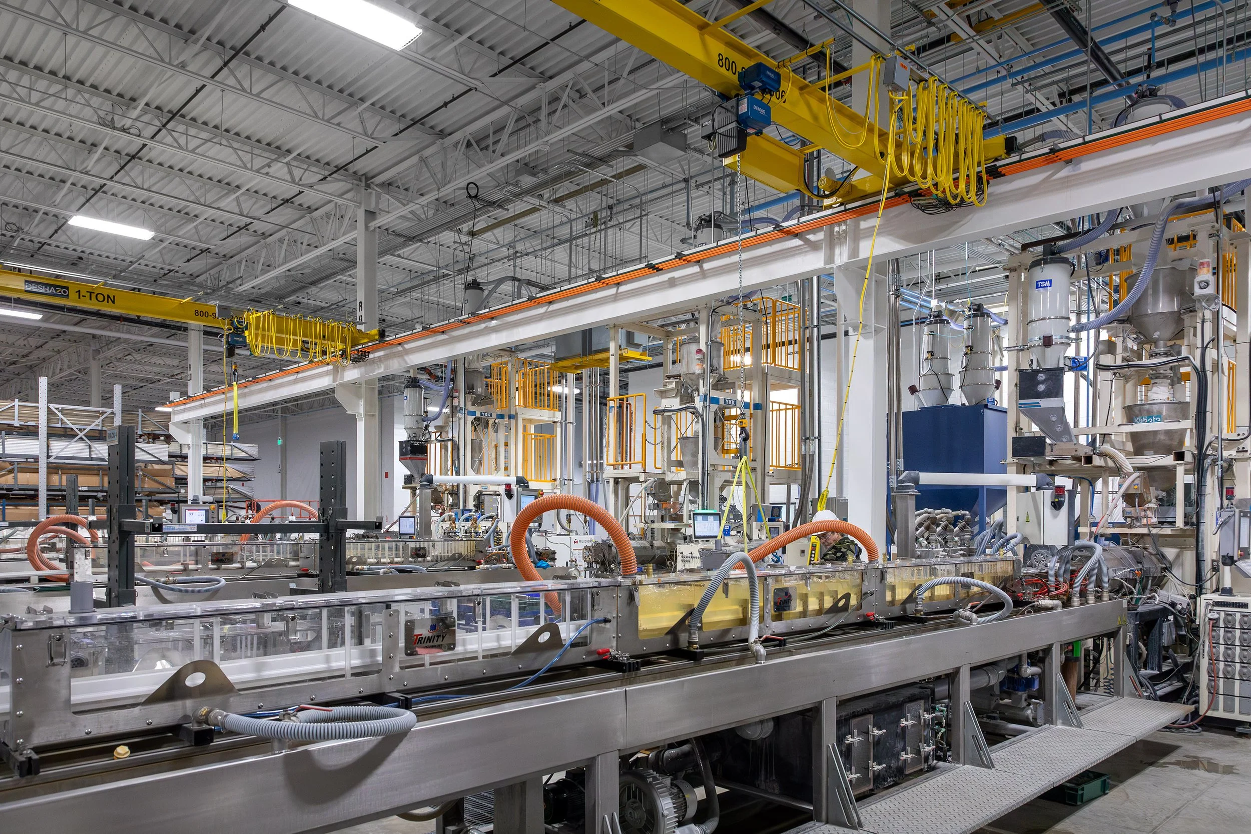 Modern industrial factory interior featuring automation, conveyor belts, and overhead cranes under bright lighting.