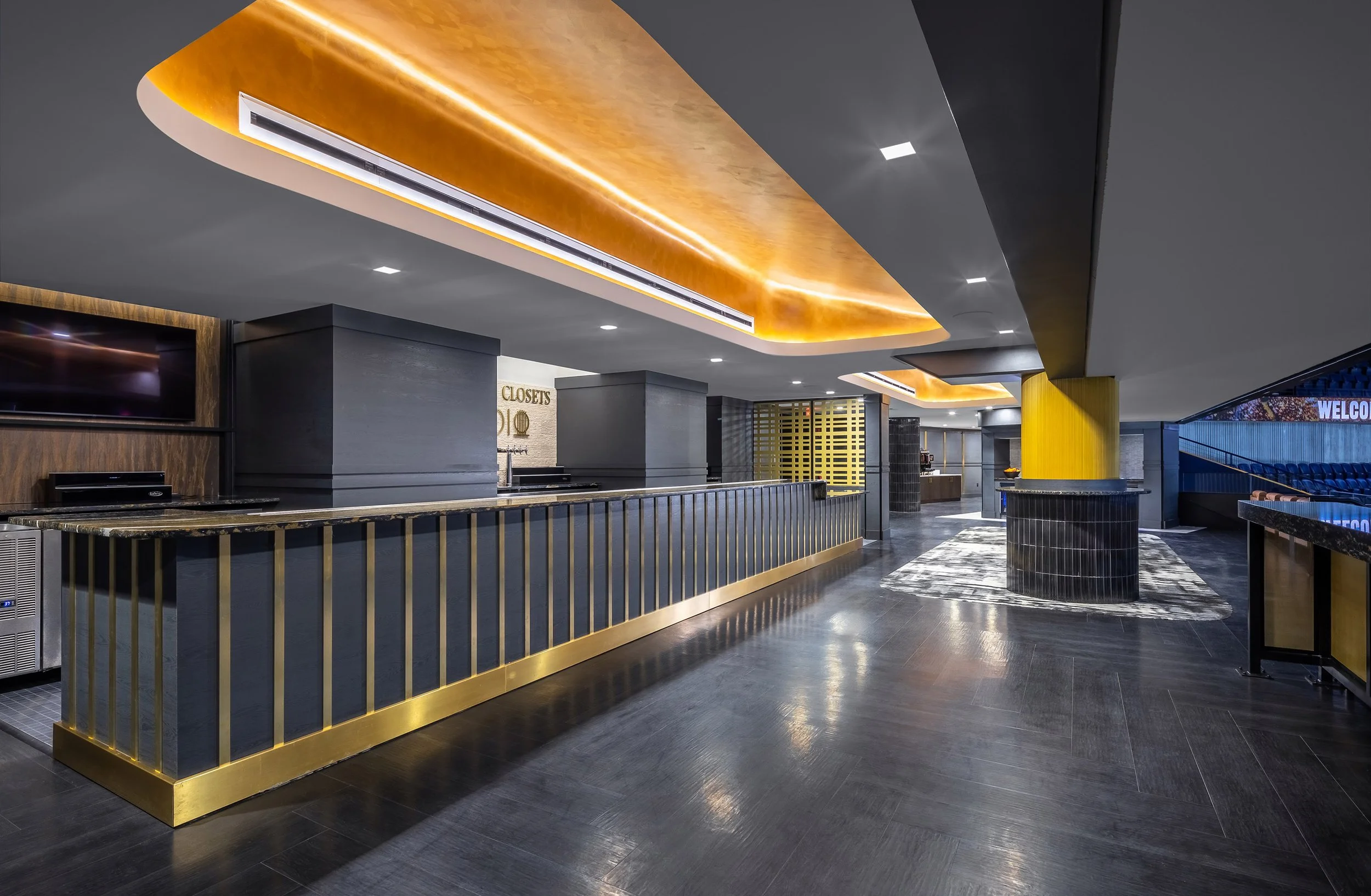 A modern bar with black and gold accents, featuring a California Closets Studio sign, marble countertops, a patterned rug, and stylish ceiling lighting reminiscent of an exclusive club within the Bridgestone Arena 114 Club.