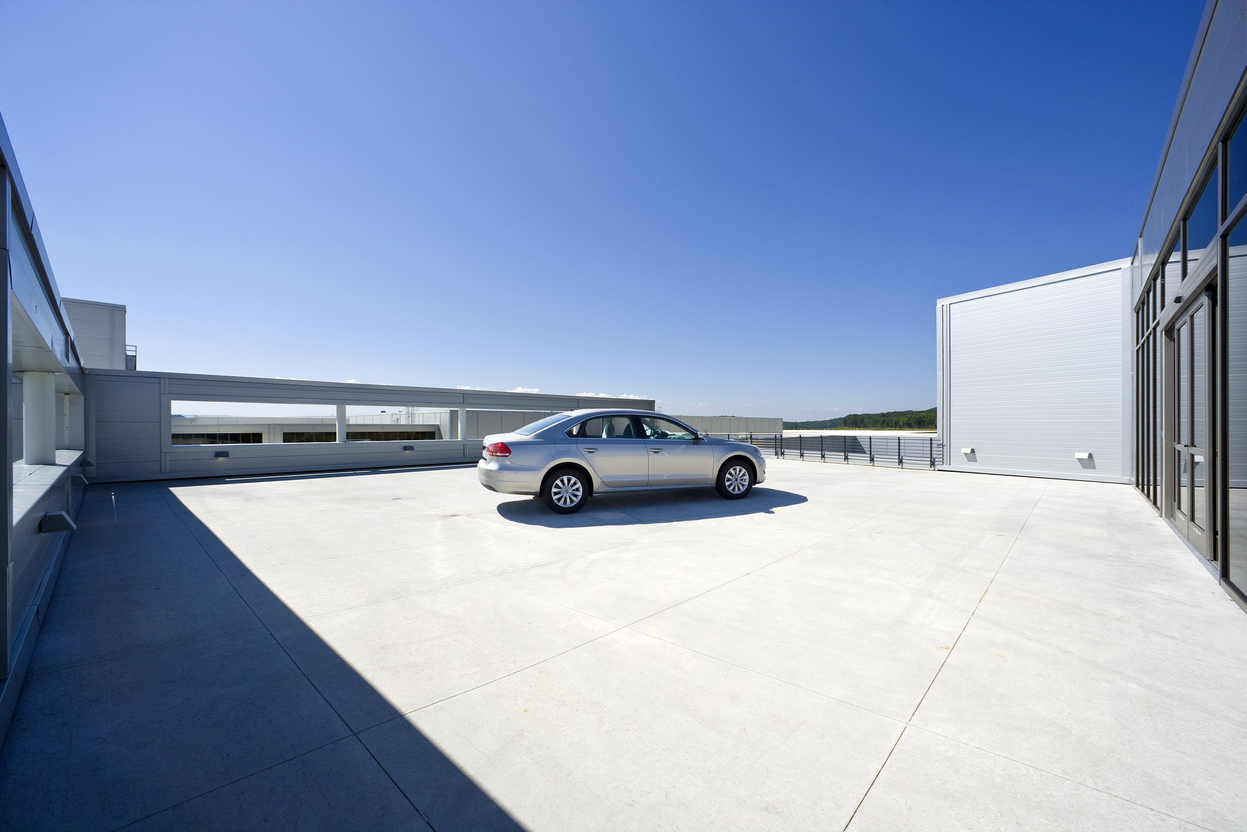 A newly produced silver Volkswagen Passat is displayed on a large, minimalist terrace beneath a clear blue sky outside Volkswagen Corporate Offices in Chattanooga, TN.