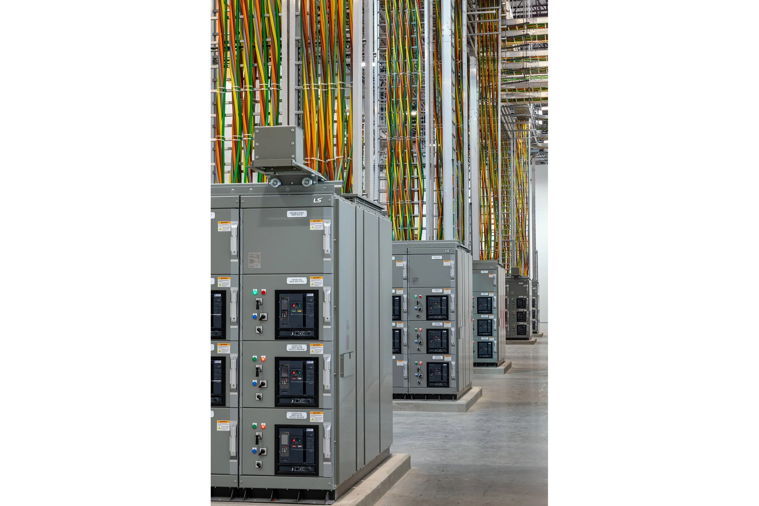 Rows of large electrical control panels line a warehouse aisle in Dallas, with many colorful vertical cables above connecting to the ceiling.