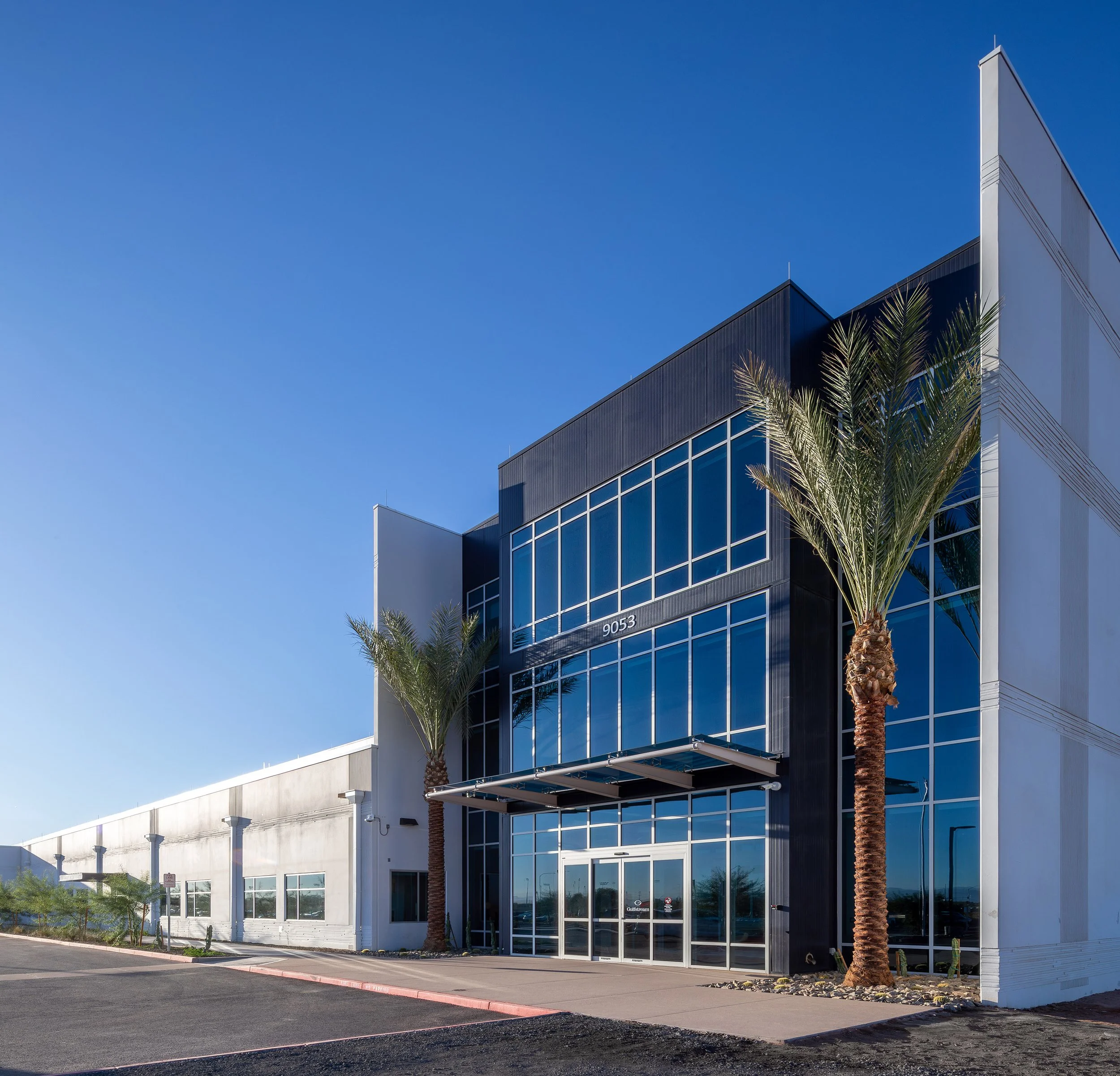 A modern architectural commercial building with large glass windows and a black-and-white facade, flanked by tall palm trees, under a clear blue sky—perfect for striking photography.