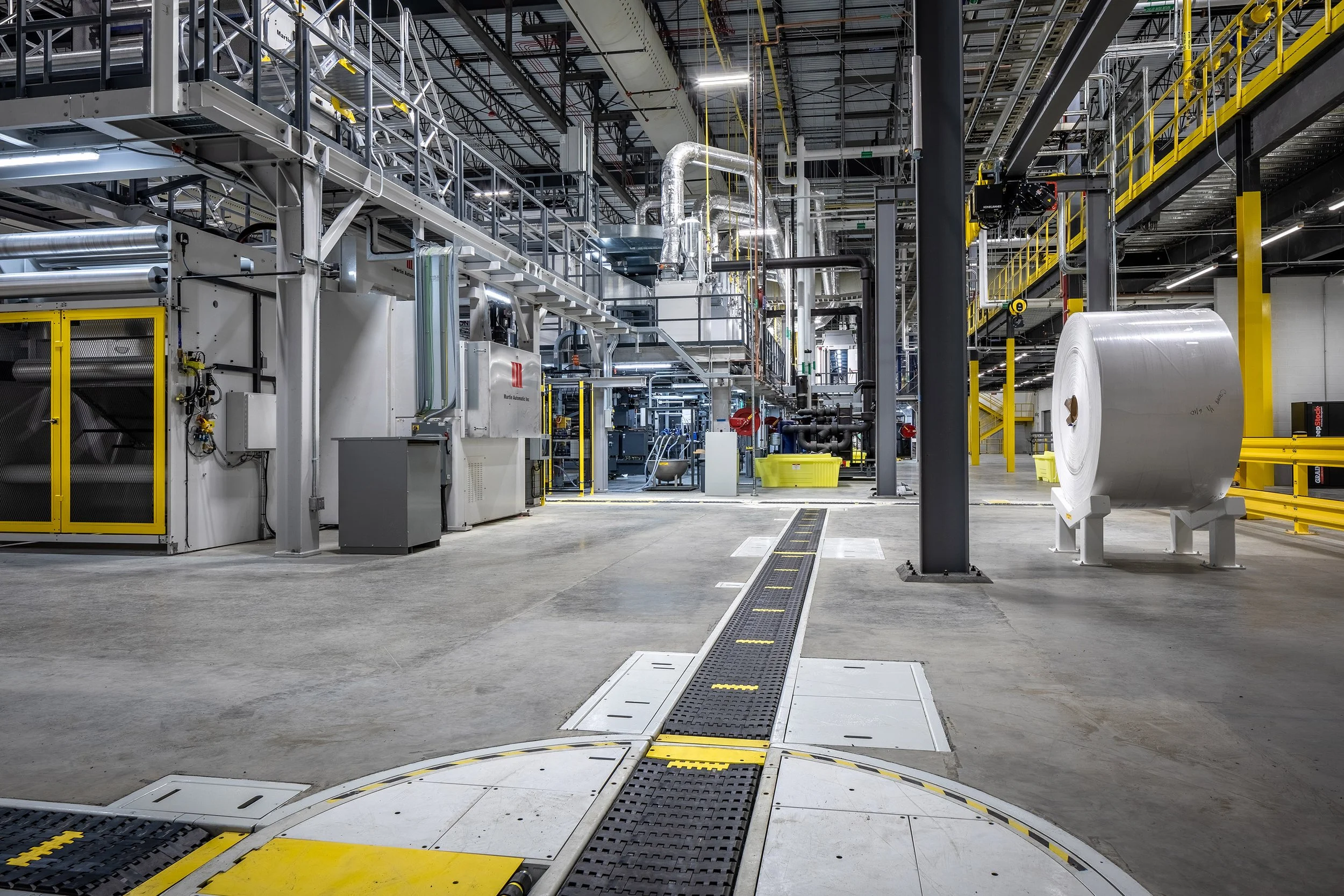 Modern Georgia Pacific manufacturing facility with machinery, overhead walkways, large material rolls, and clean, organized floors.