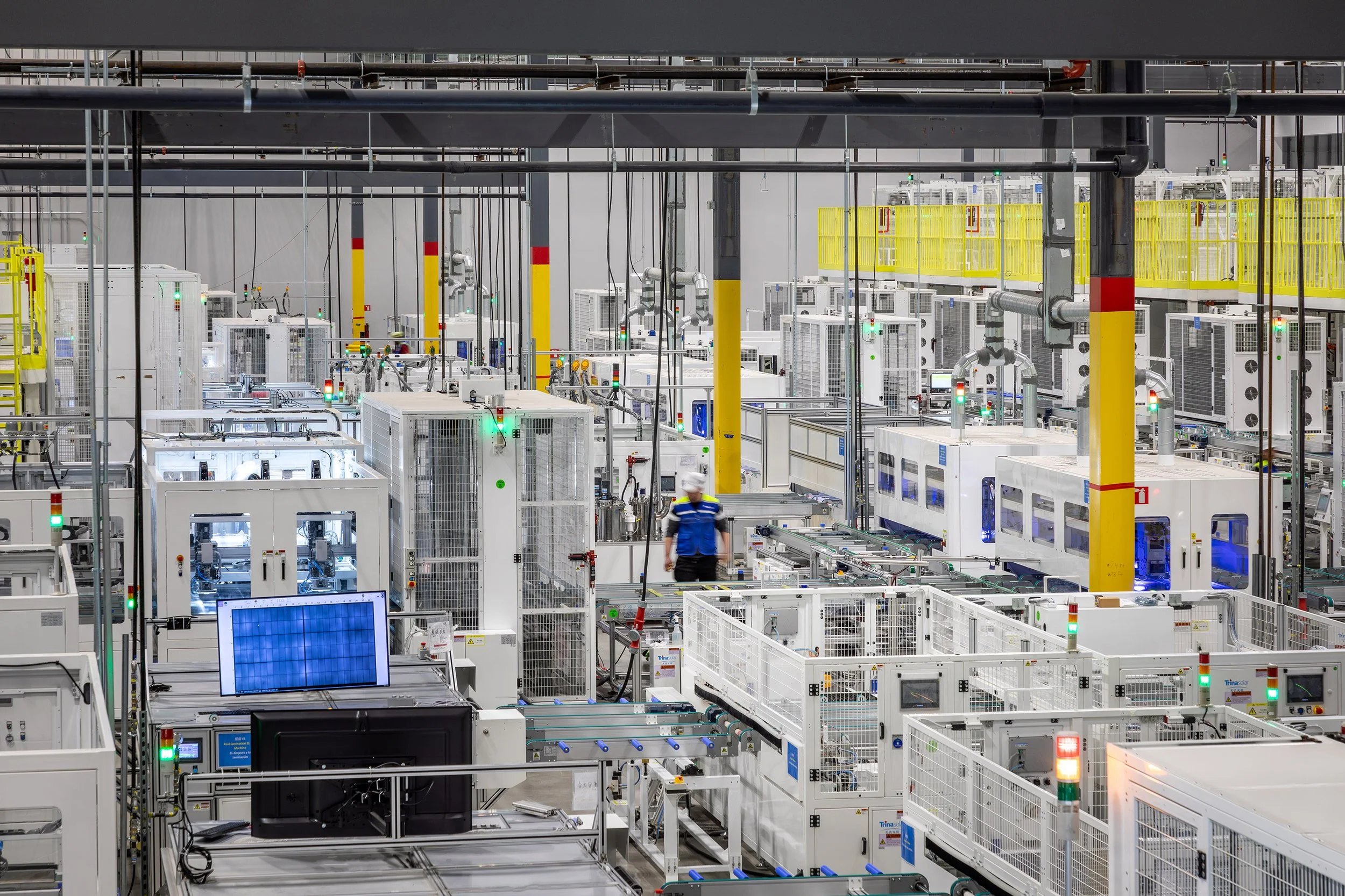 Elevated view of a modern industrial facility in Dallas features automated machines, conveyor belts, and computer monitors displaying process data amid yellow railings and structural columns.