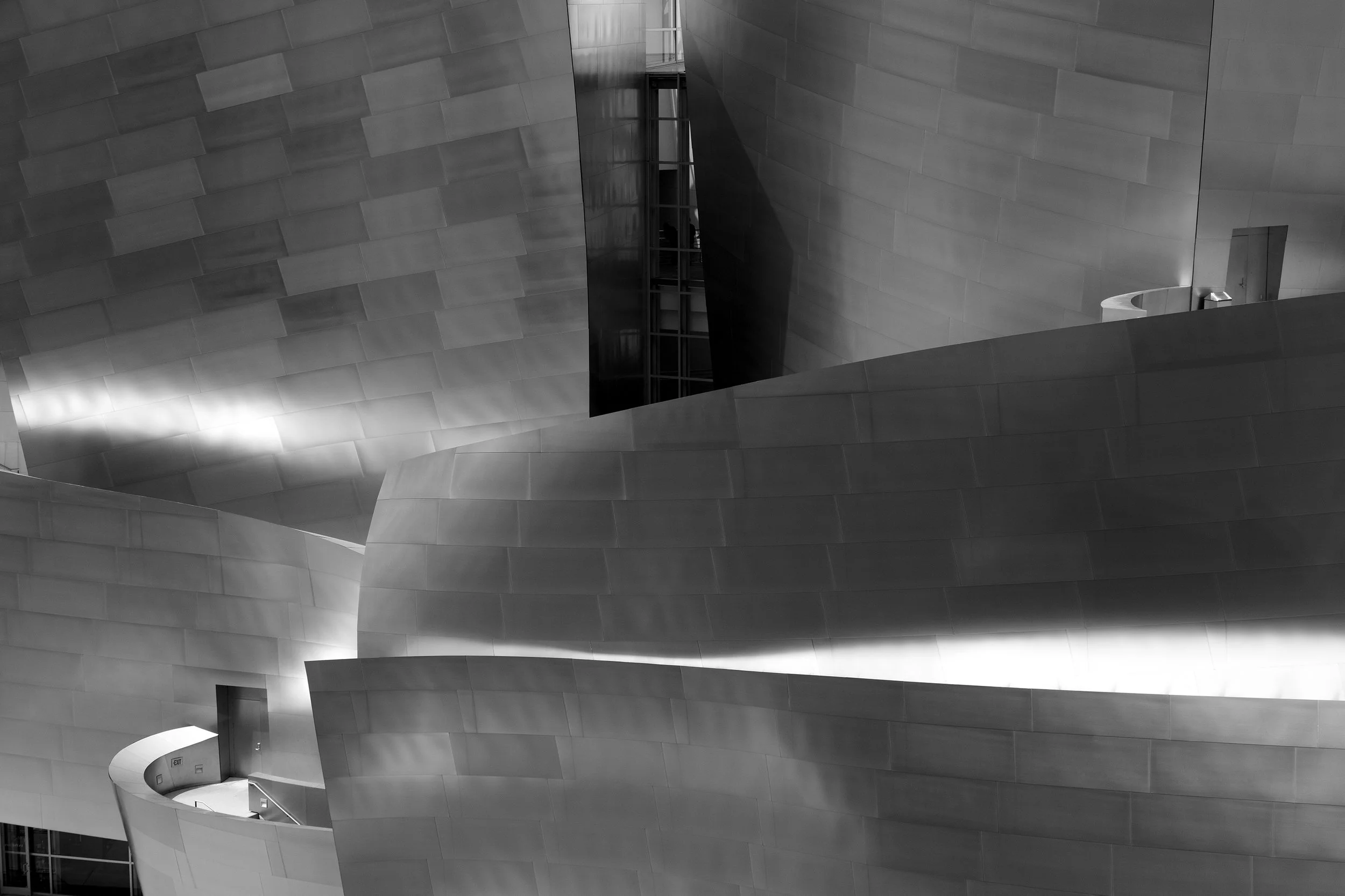 Curved, reflective metal walls and railings form an abstract architectural scene in black and white.