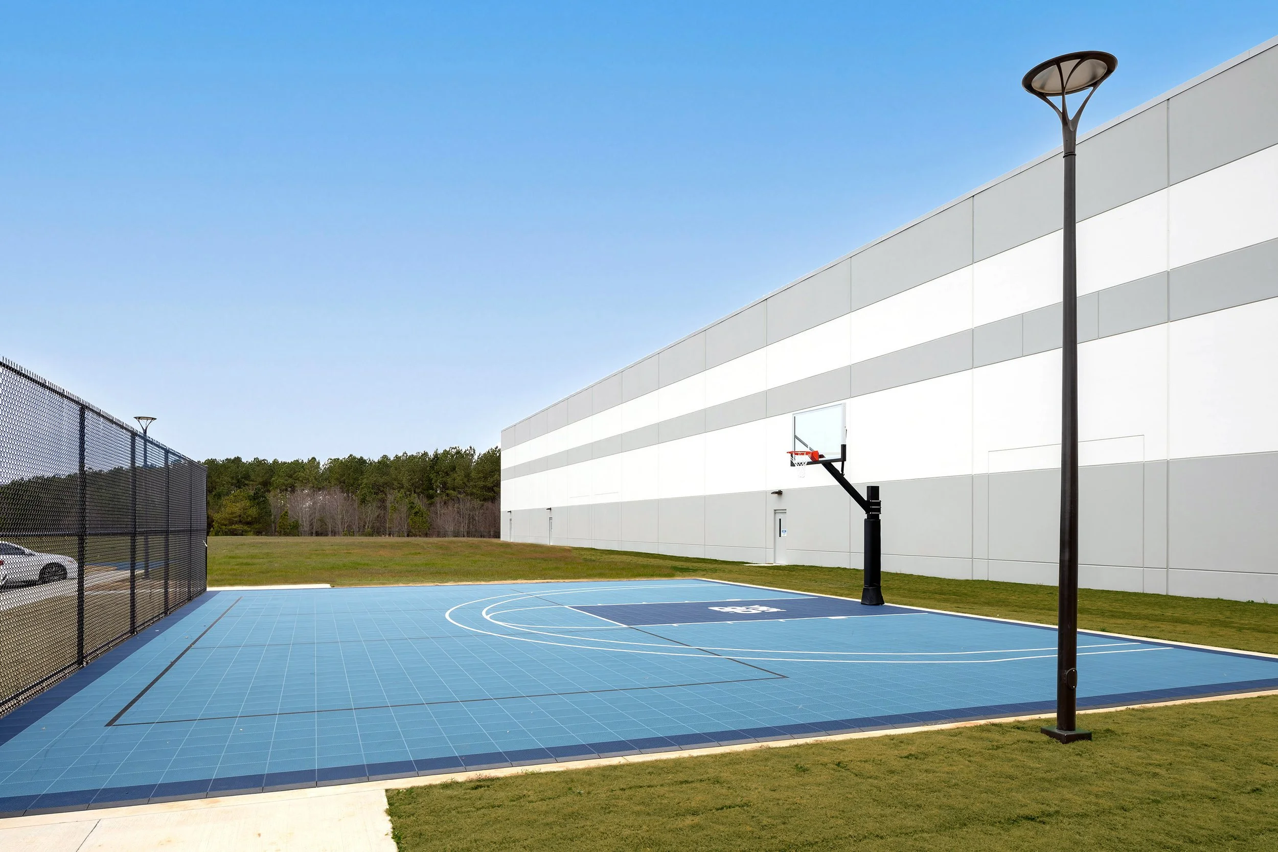 Outdoor basketball court with blue flooring in Macon, Georgia, beside a modern building under a clear sky.