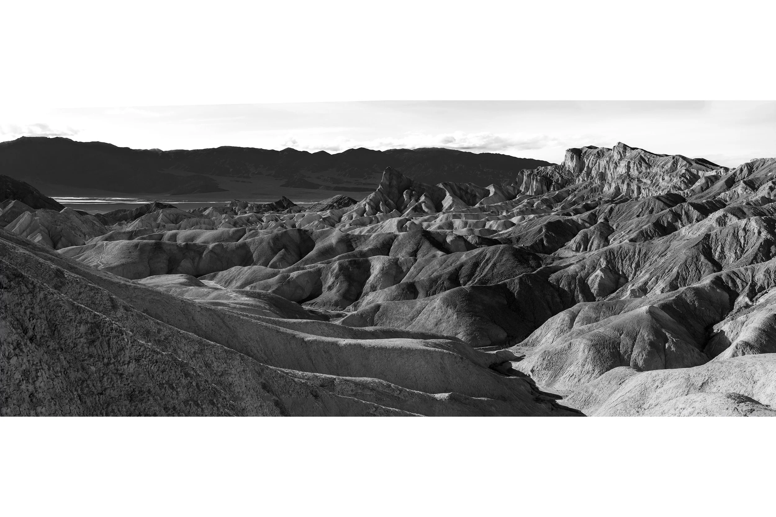 Black and white photo of rugged Death Valley hills and mountains beneath a bright desert sky at Zabrieski Point.