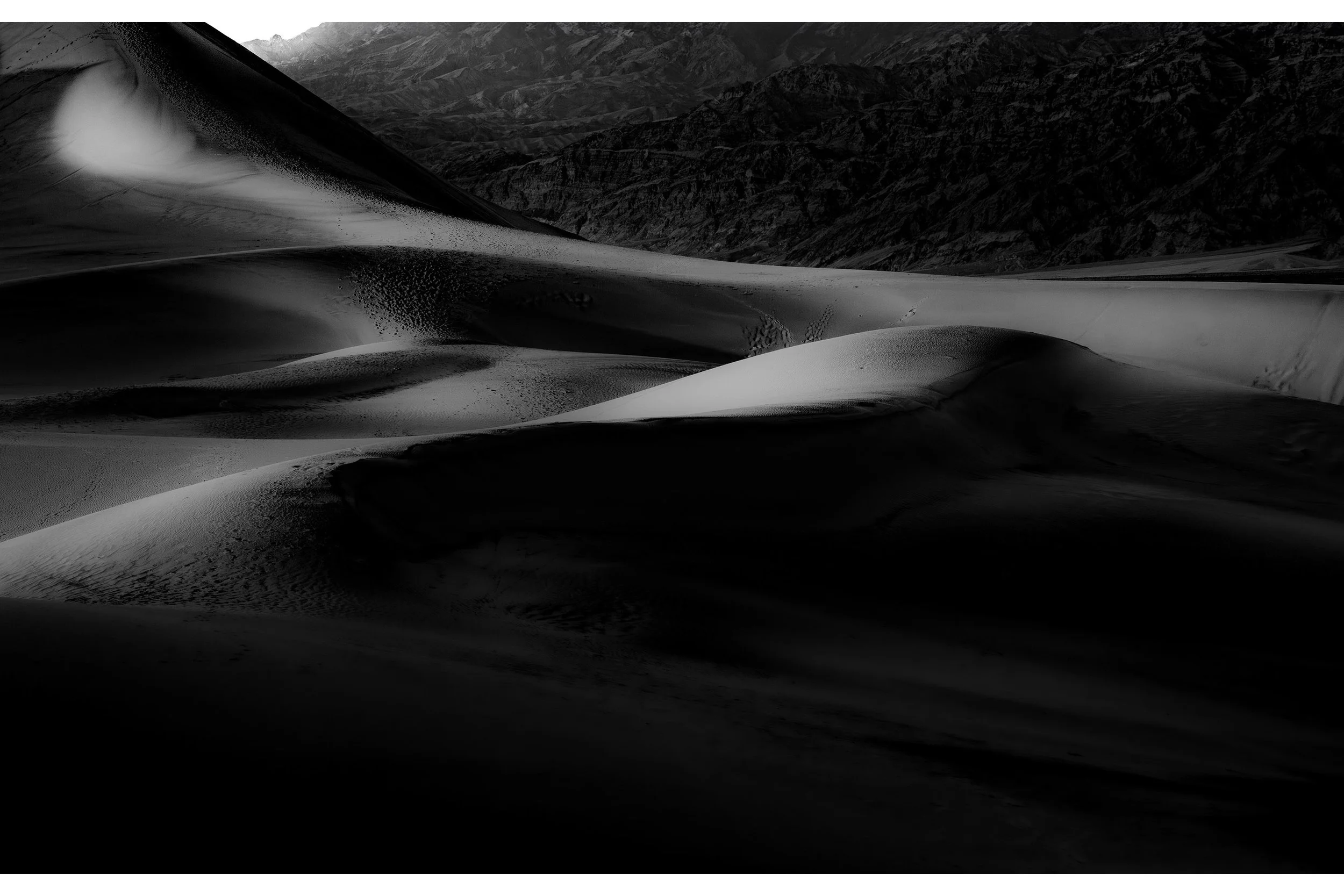 Black and white photo of Death Valley sand dunes, showcasing dramatic shadows and textured ridges under soft light.
