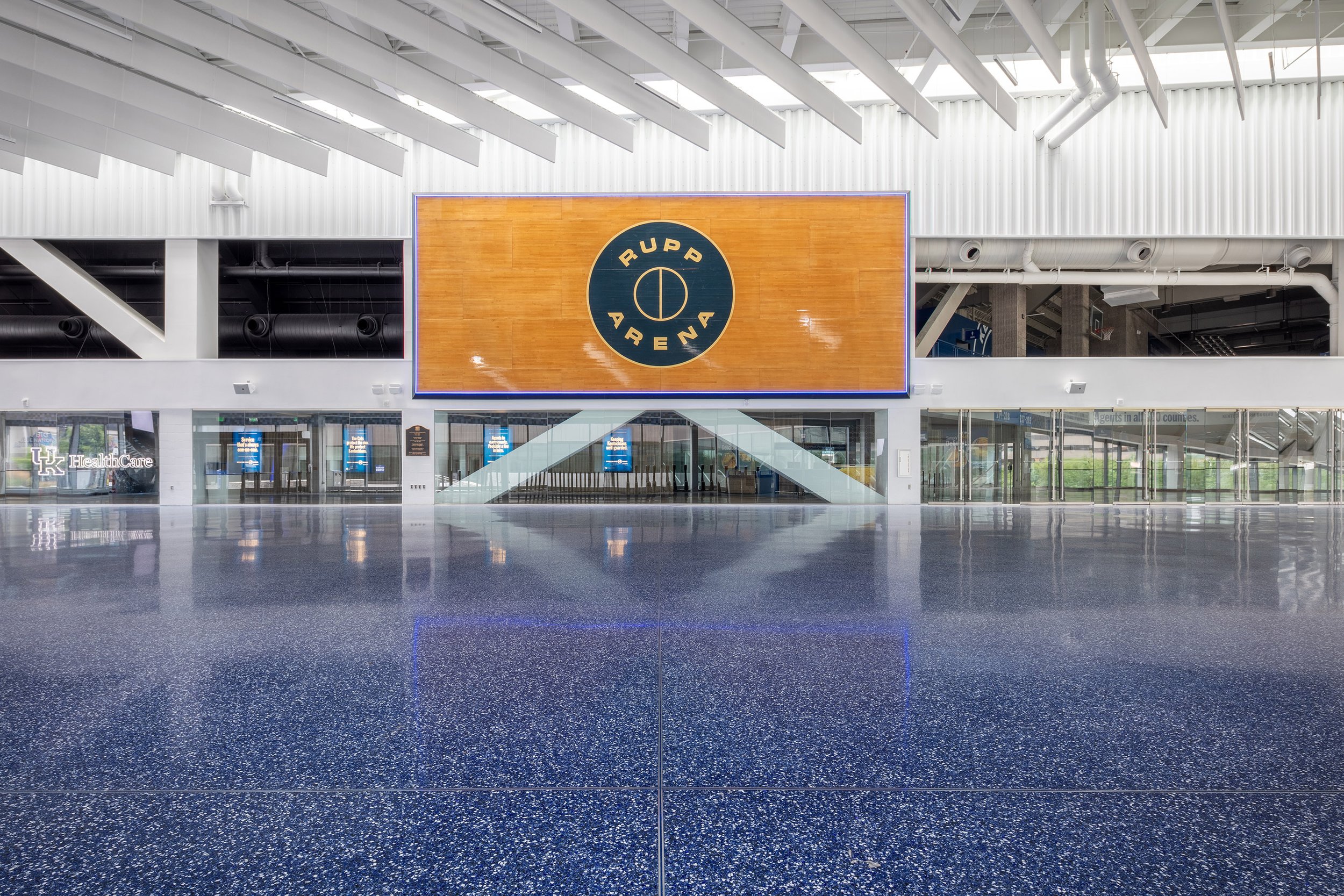 Large indoor area with terrazzo floors, glass doors, and a wooden wall display reading Rupp Arena in the center.
