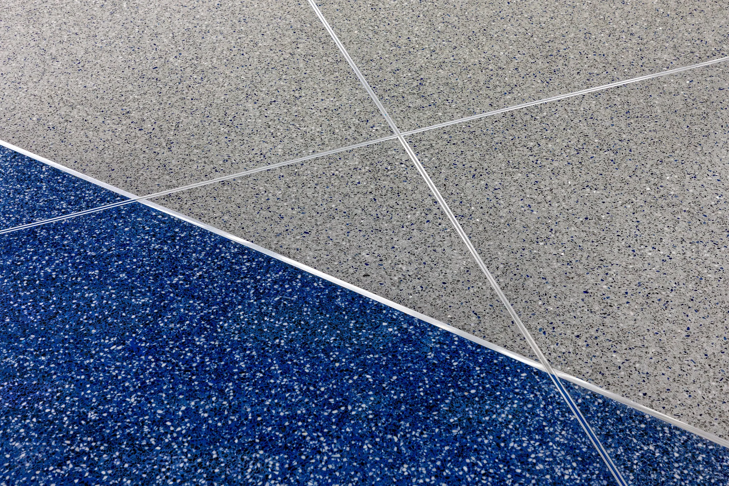 Close-up of a speckled floor at Rupp Arena, with intersecting silver lines—a nod to modern architecture and tradition.