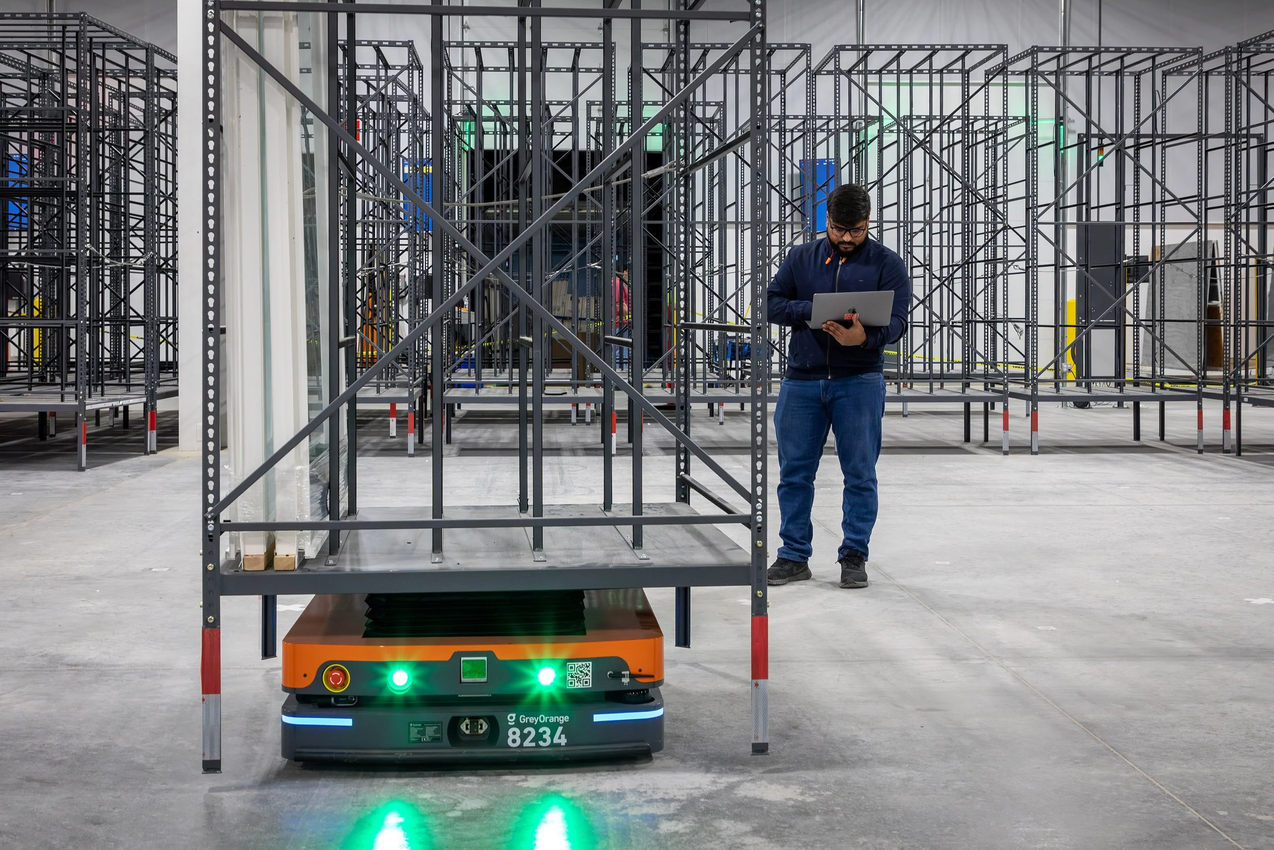 An engineer with a laptop monitors an orange robot moving product shelves in a Macon warehouse.