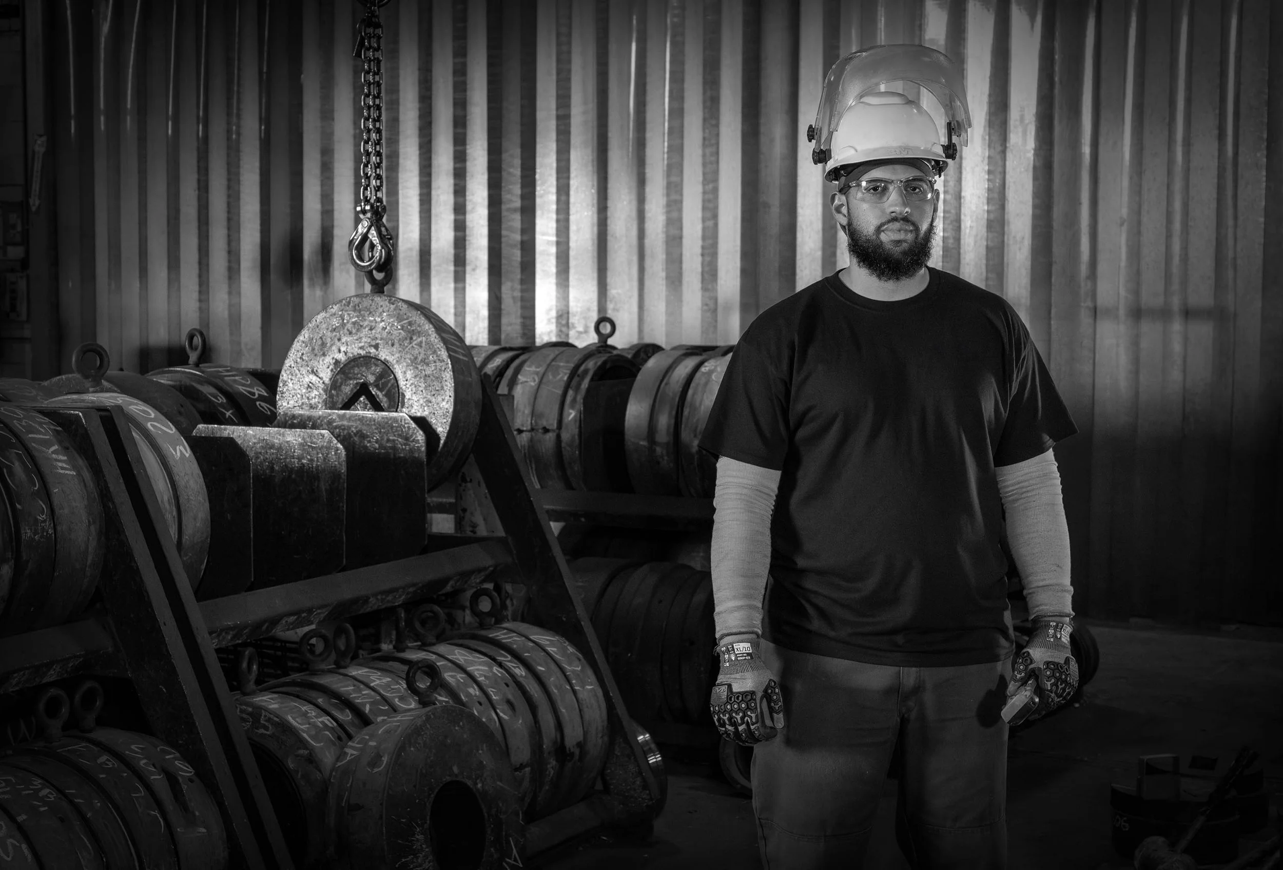 A worker in safety gear stands in an industrial setting with large metal coils, captured in striking black and white.