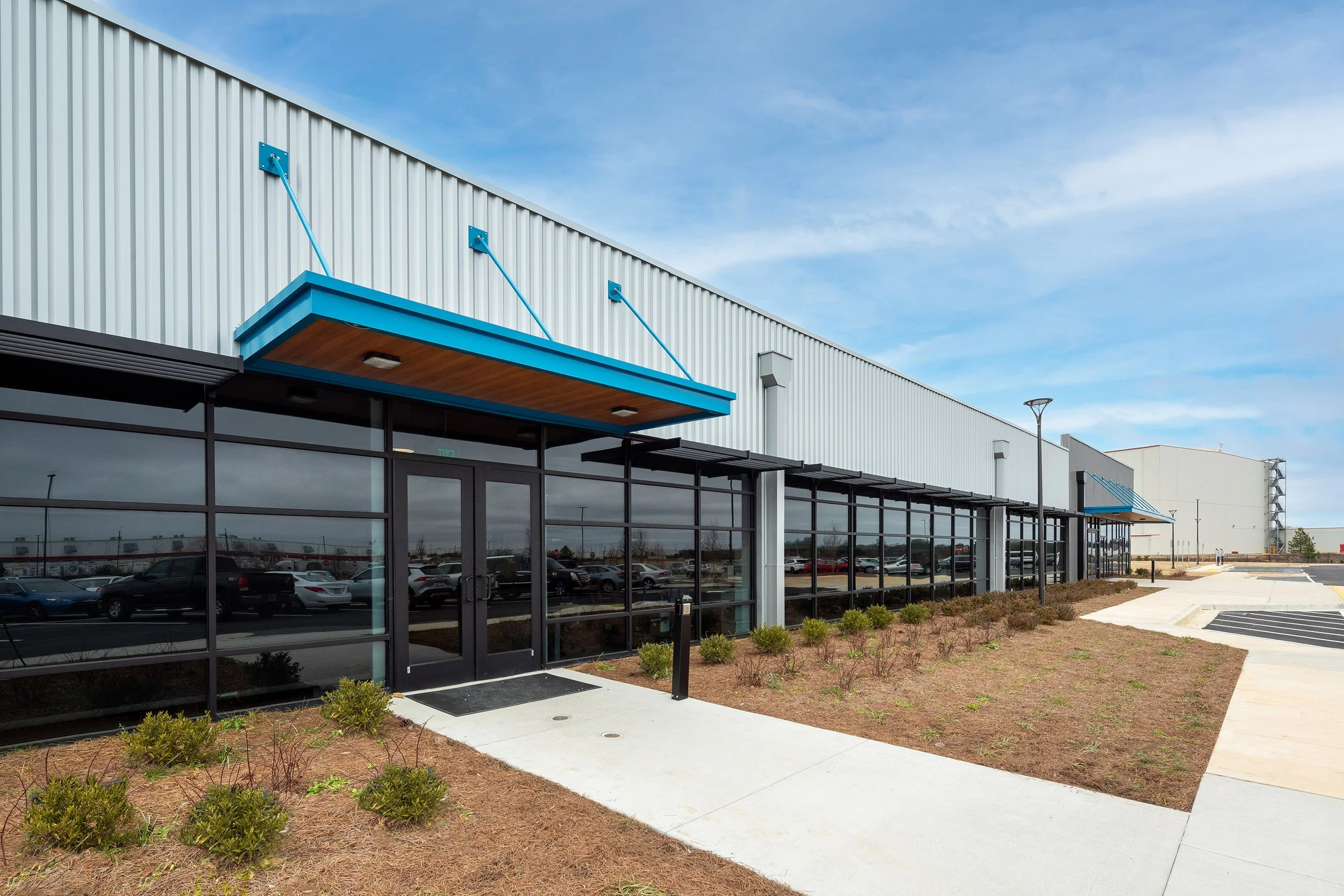 Modern industrial building in Georgia with large windows, blue awnings, and a landscaped walkway under a clear sky.