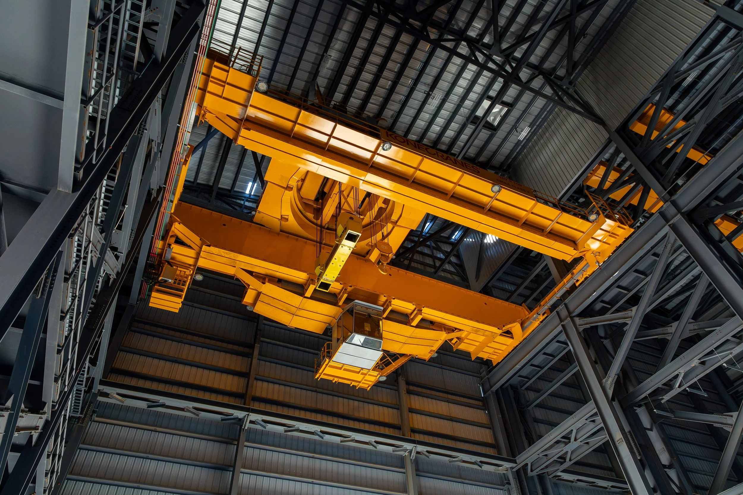 A large yellow overhead crane inside an industrial warehouse, viewed from below, with metal beams and a corrugated roof visible in the background—ideal for handling heavy metals during the recycling process.