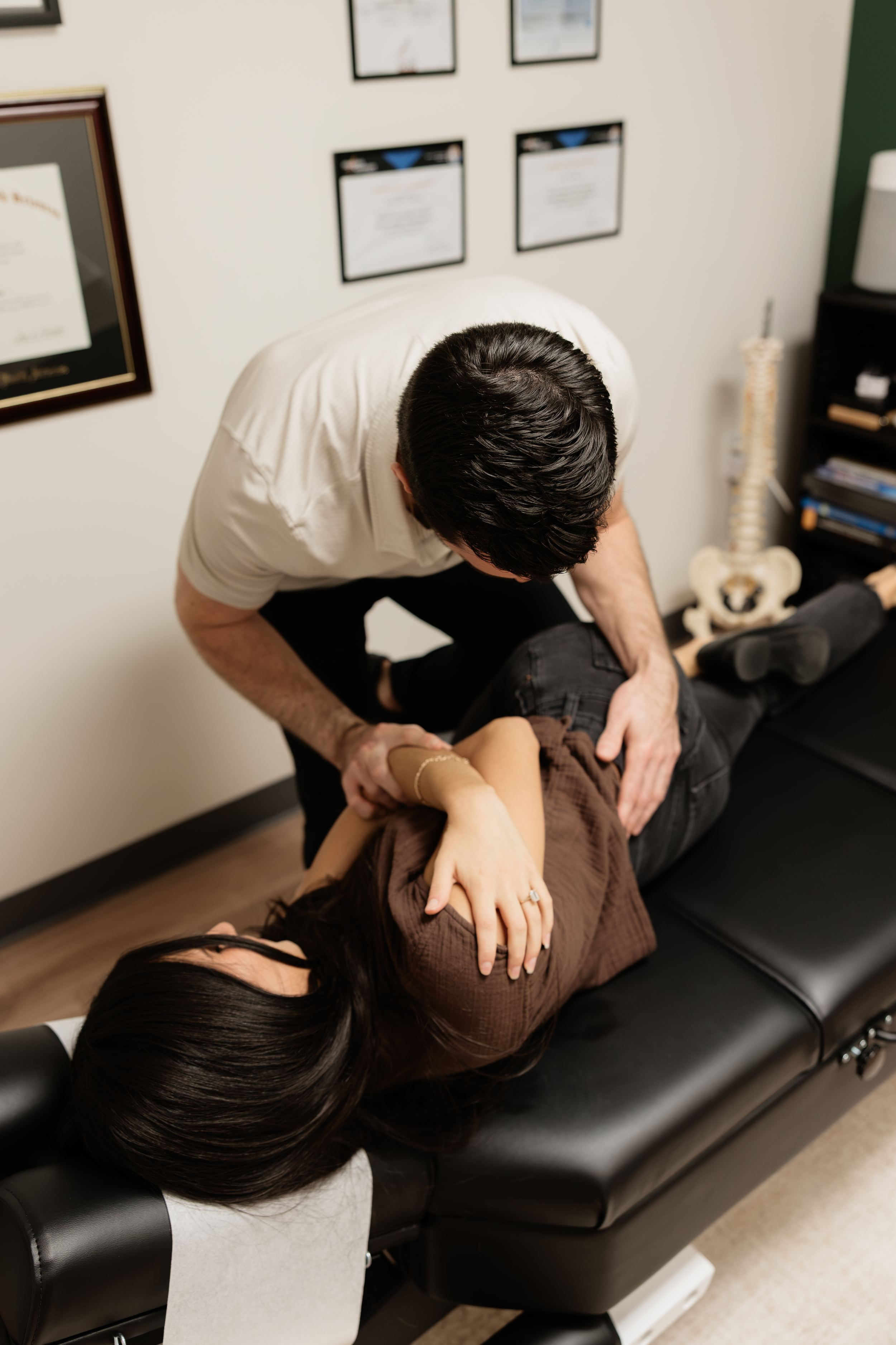 A chiropractor adjusting a patient lying face down on a chiropractic table in a medical office.